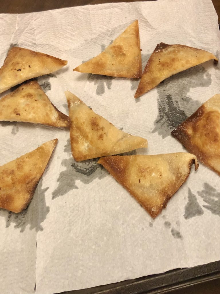 fried crab rangoons that have been removed from the skillet and transferred to a paper towel lined plate to absorb the excess oil