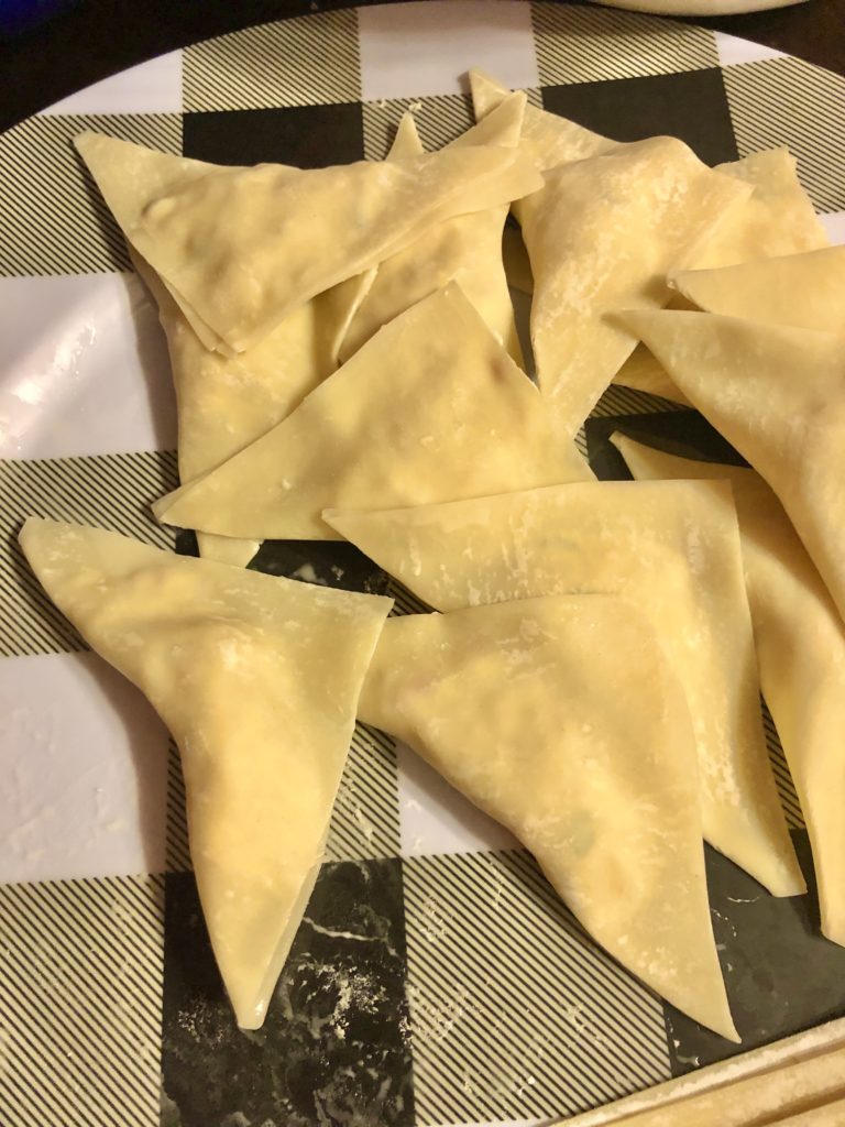 black and white plaid plate full of prepared crab rangoons that are ready to be fried
