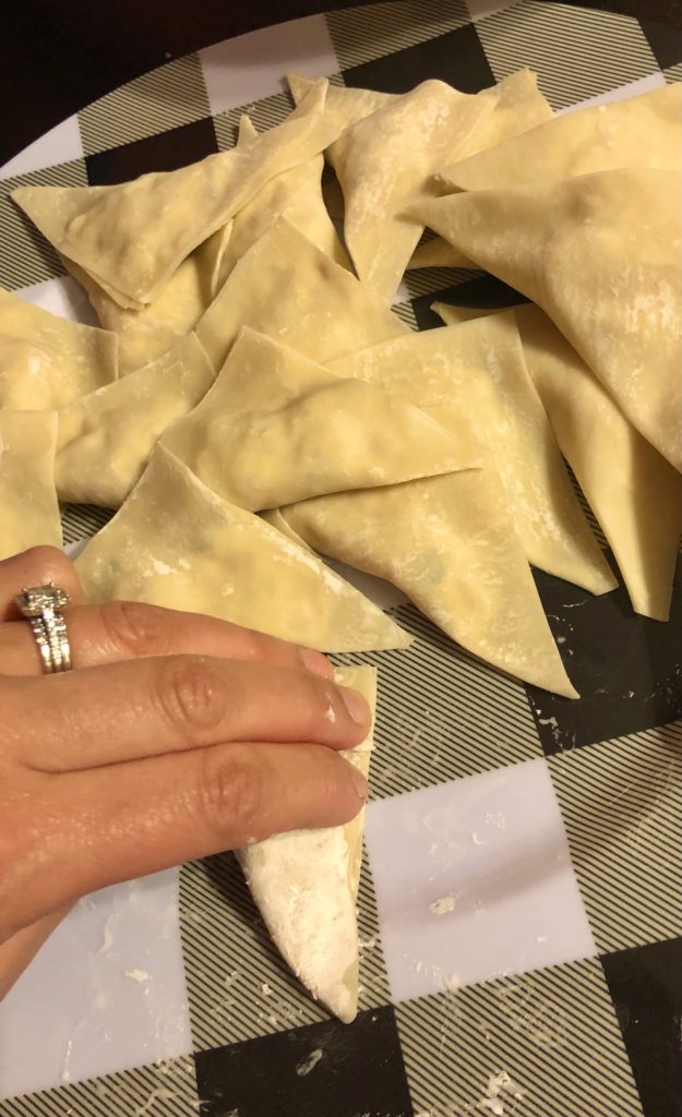 prepping crab rangoon on black and white plate. a hand is pressing and sealing the edges of a crab rangoon