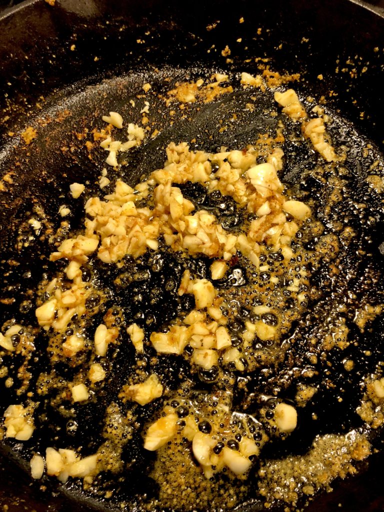 adding olive oil and garlic to cast iron skillet that the cajun shrimp was cooked in