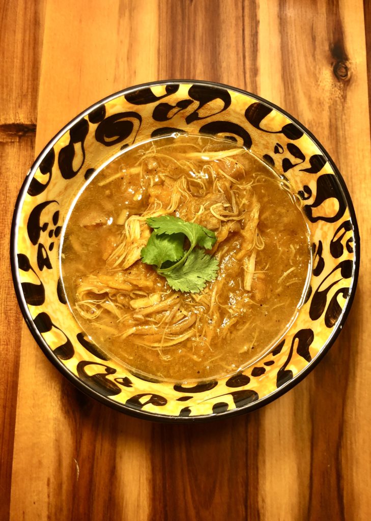 slow cooker curry chicken and sweet potato bone broth soup in leopard print bowl and garnished with cilantro in the middle. The bowl is on top of a wooden cutting board