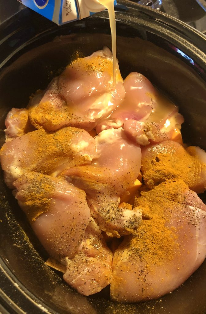 chicken bone broth being poured into slow cooker pot with chicken, sweet potatoes, curry powder and other seasonings.