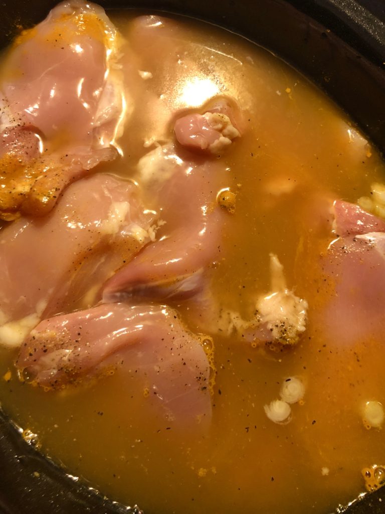 raw boneless skinless chicken breast in curry bone broth soup about to be cooked in crockpot