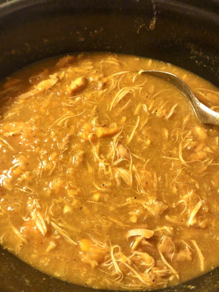 slow cooker curry bone broth soup being stirred in crockpot with silver spoon. The soup is being stirred to break apart the slow cooked chicken and sweet potatoes.