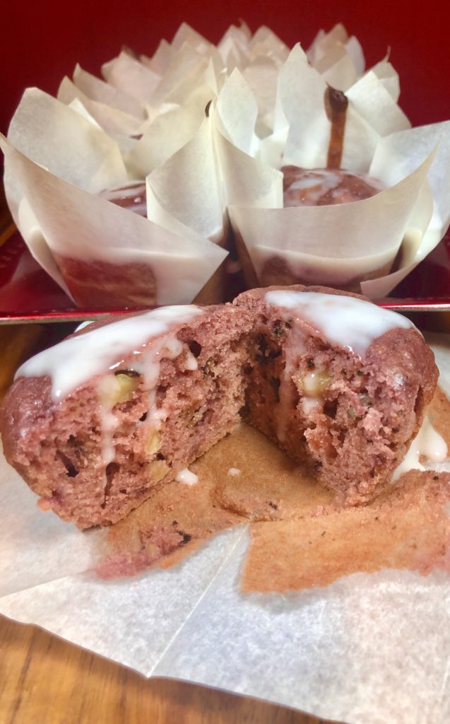 One strawberry bread muffin with lemon glaze sliced in half in front of red plate with other muffins