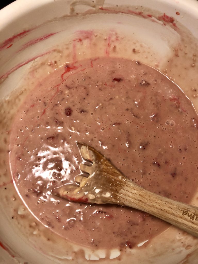 strawberry and walnut quick bread batter in large white mixing bowl being stirred with wooden spoon