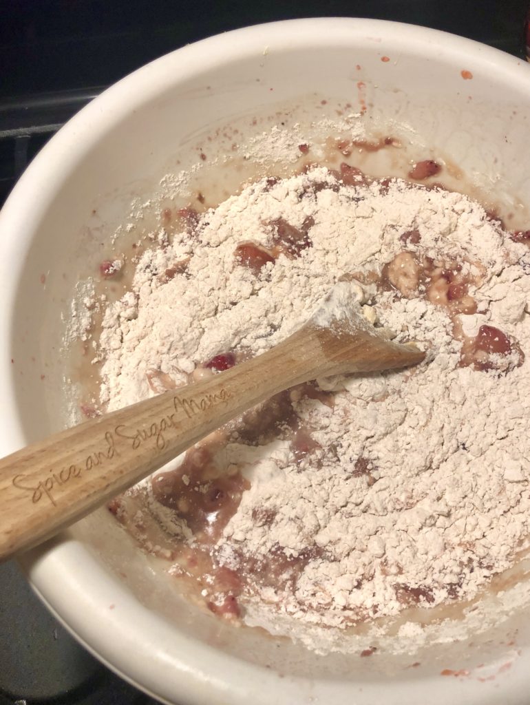 strawberry bread batter with flour added in large white mixing bowl and wooden spoon