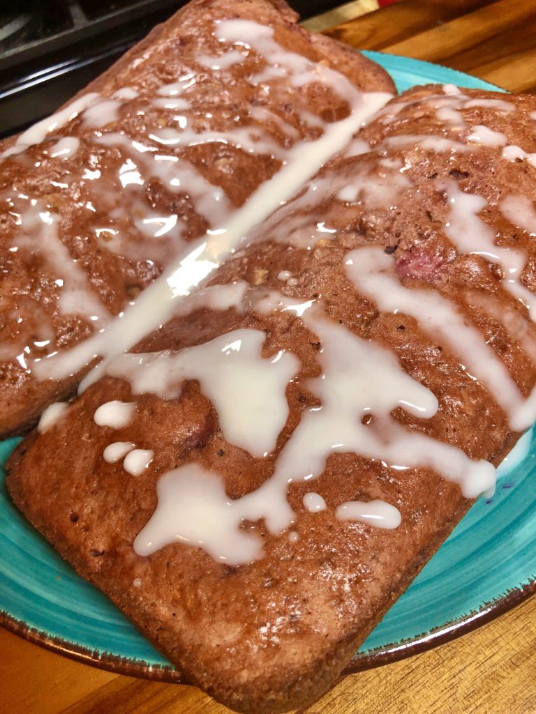 two strawberry bread with walnut loaves covered with lemon glaze on light blue plate on top of wooden cutting board