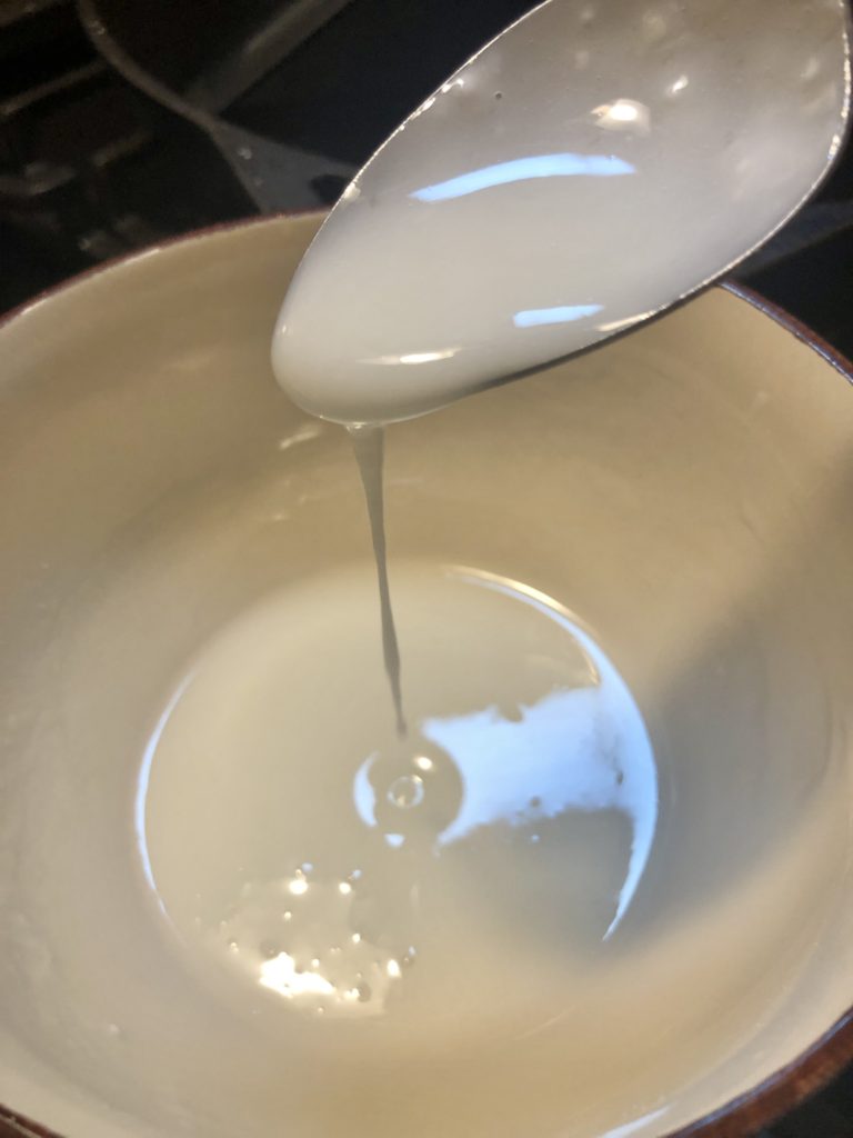 lemon glaze in small bowl with spoon drizzling glaze back down into the bowl