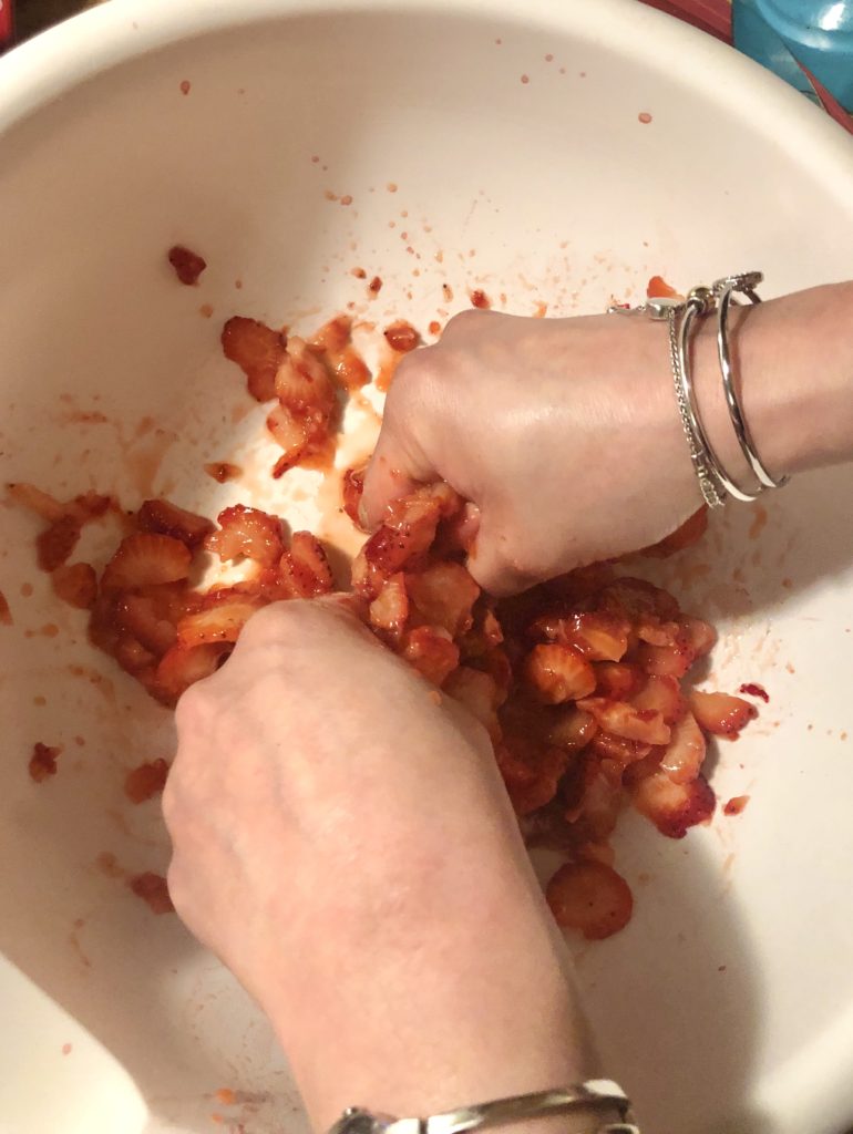 hand mashing strawberries in large white mixing bowl