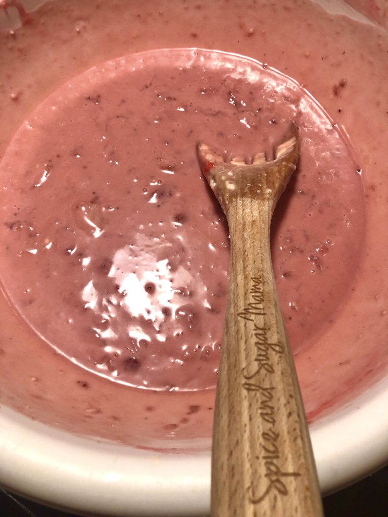 strawberry walnut quick bread batter stirred with pink gel food coloring in white mixing bowl and wooden spoon