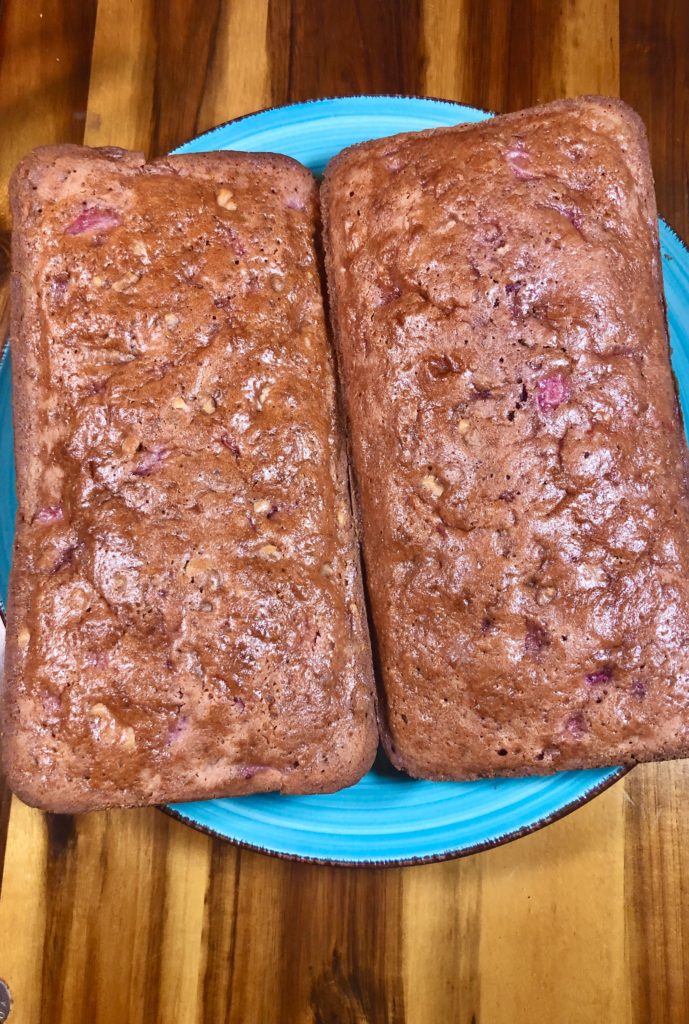 two strawberry quick bread with walnut loaves cooling on blue plate on top of wooden cutting board
