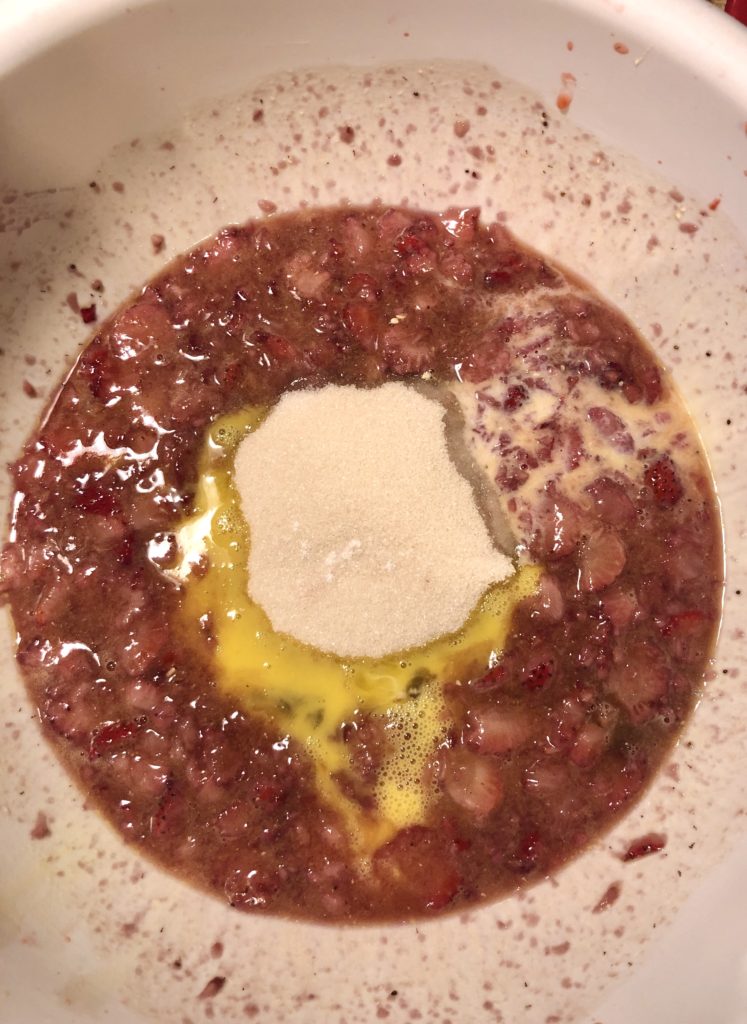 strawberry bread batter in large white mixing bowl with vanilla extract, milk, sugar and egg added