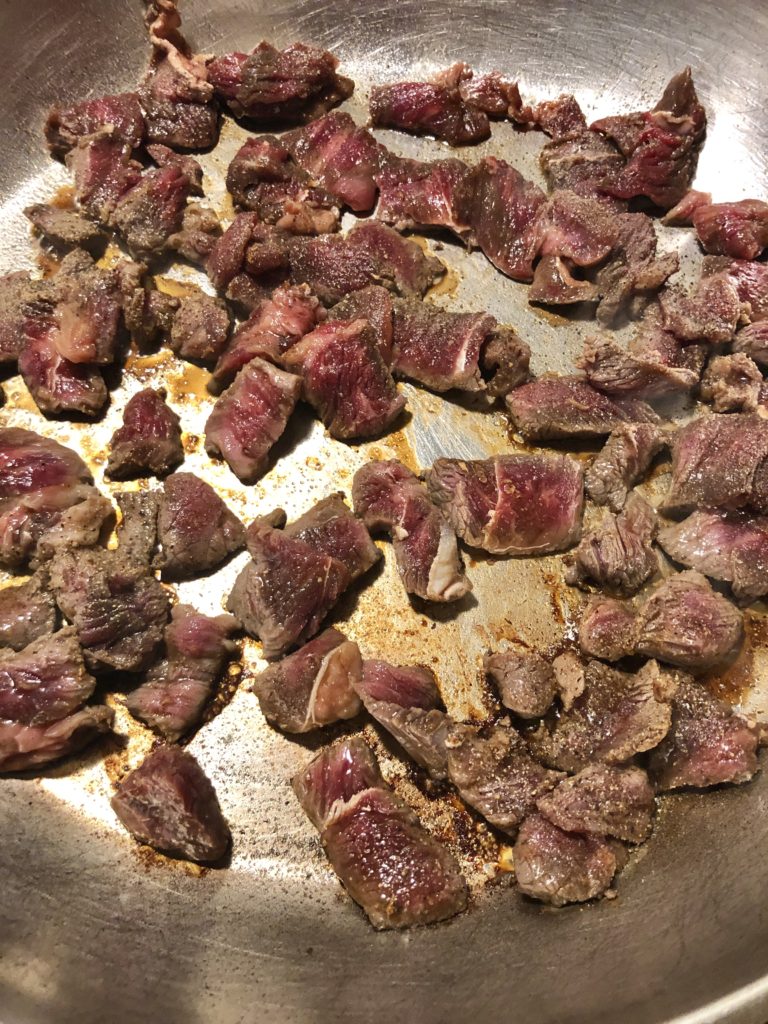 Thai marinated beef frying in large silver pan