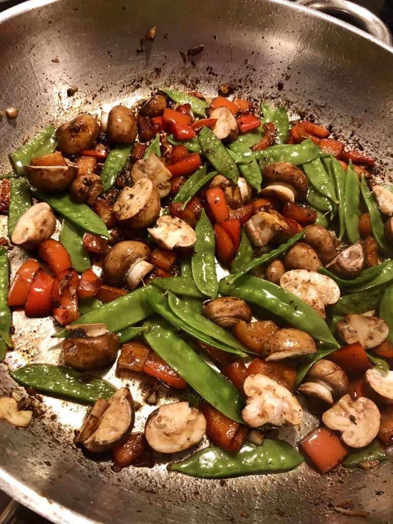 red bell peppers, garlic, Thai chili peppers, mushrooms and snow peas frying in large silver skillet