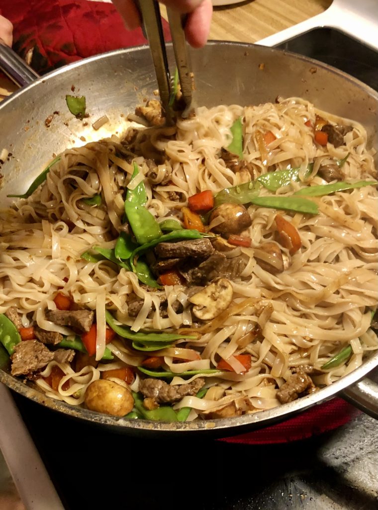 Thai beef noodles with snow peas, mushrooms and red bell peppers being stir fried together in large skillet