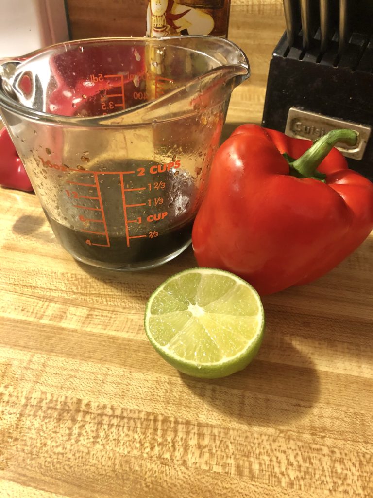 stir-fry sauce pictured in measuring glass pictured next to whole red bell pepper and half of a lime.