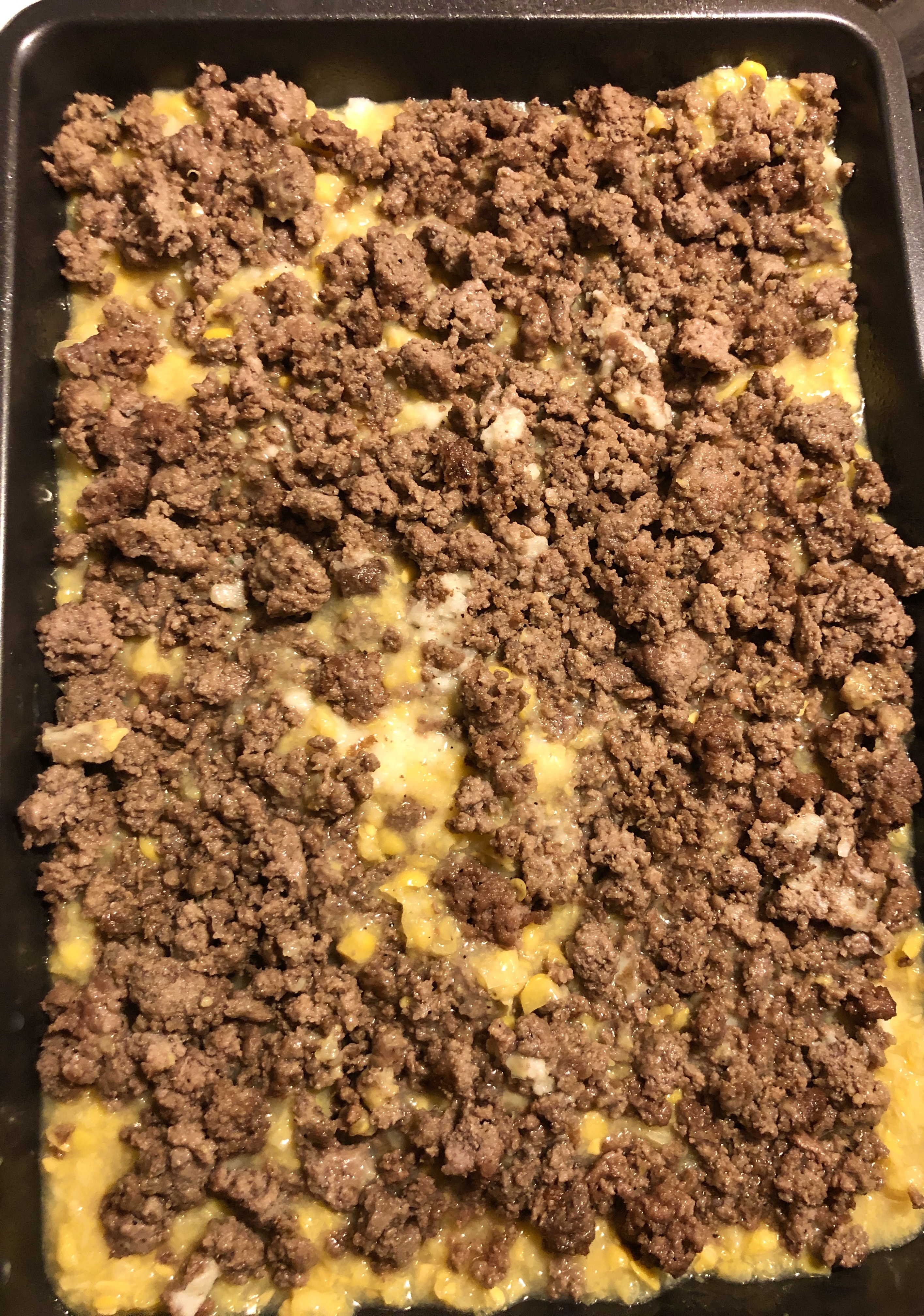 Shepherd's Pie being assembled in baking pan. The ground beef has been added over the layers of mashed potatoes and canned cream corn.