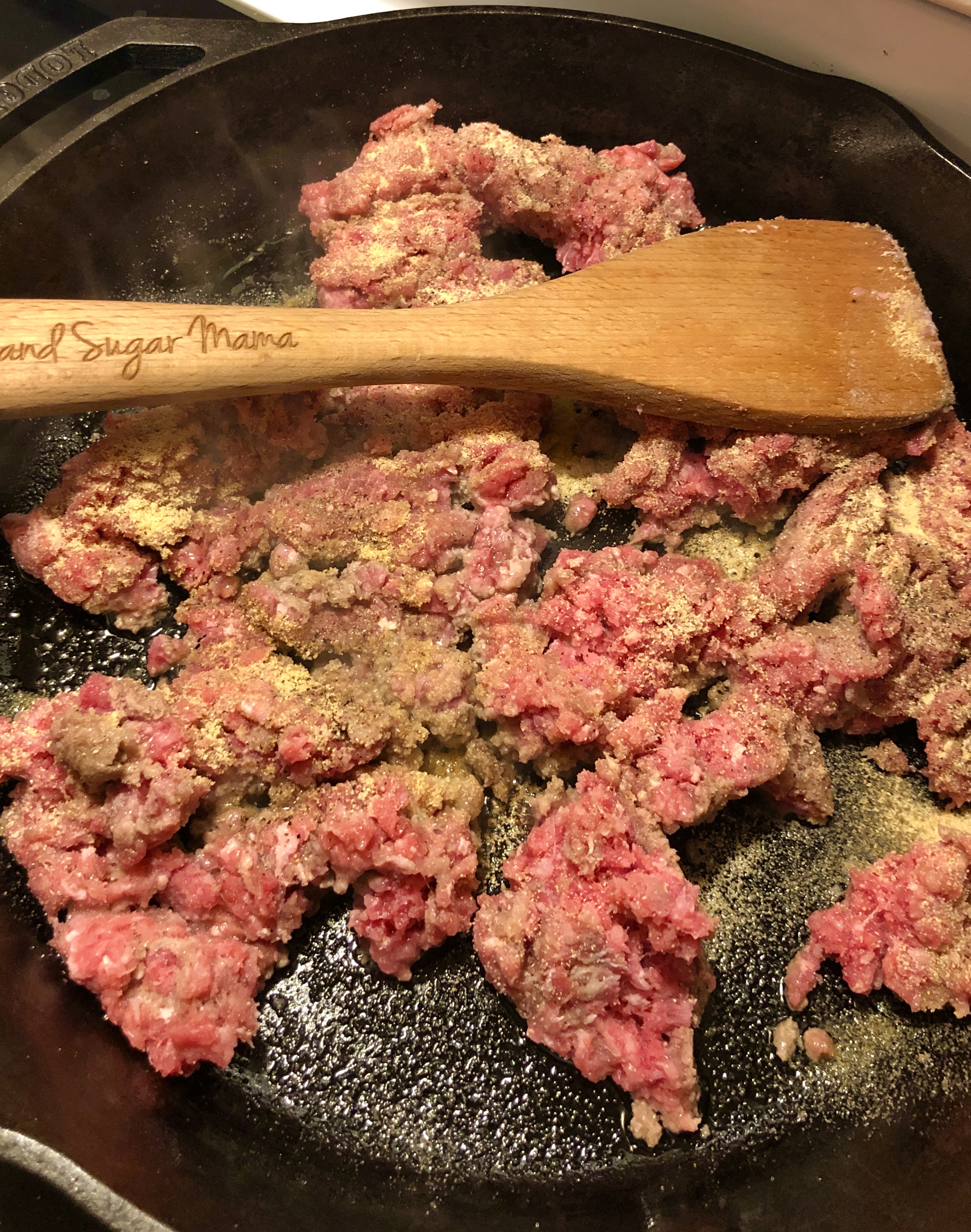 Ground beef being browned in skillet and stirred with a wooden spoon.