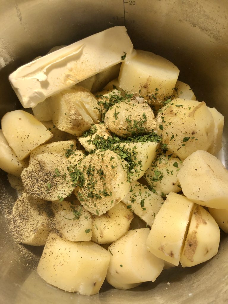 Boiled potatoes, seasonings, butter and milk in a silver pot before mashing.