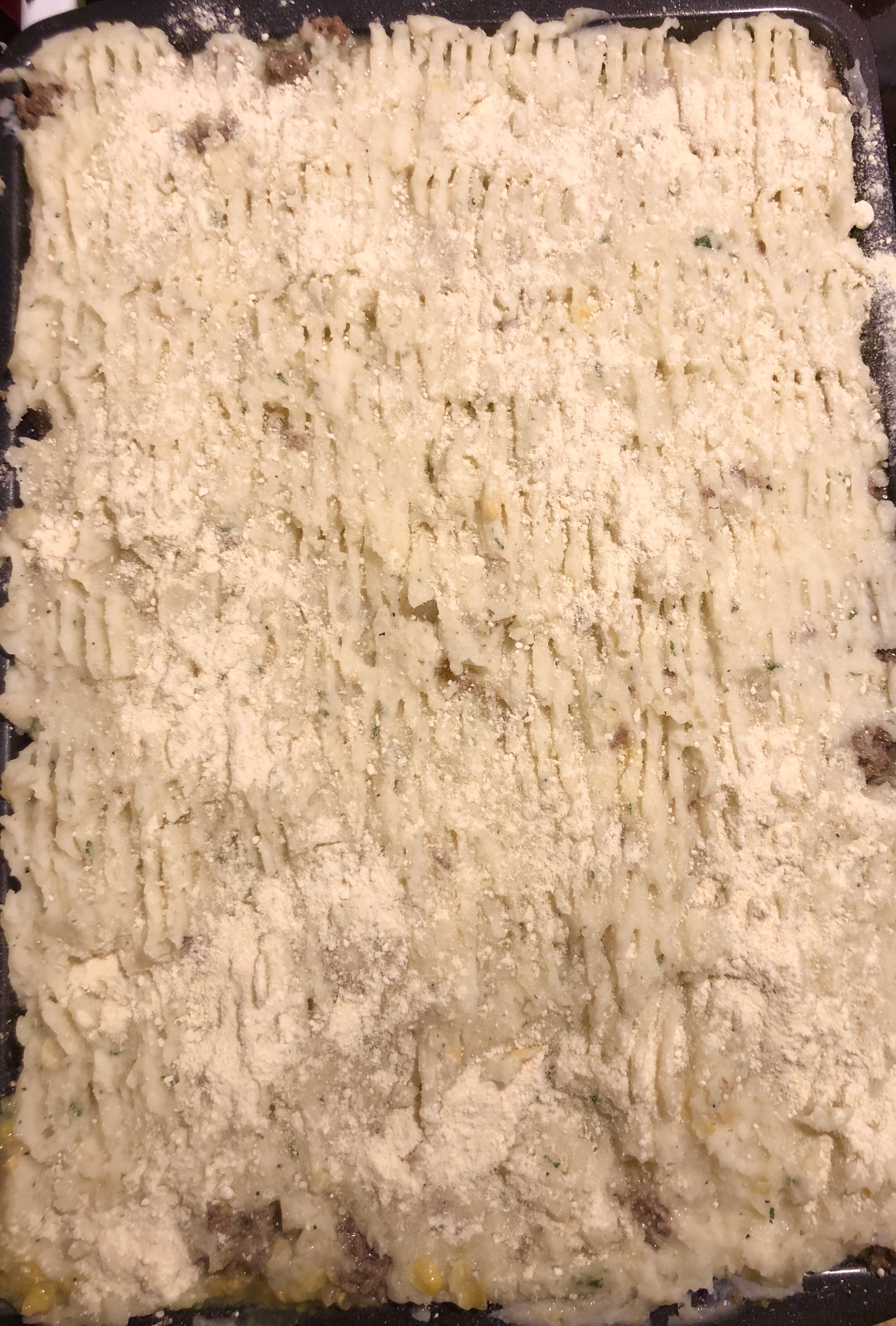 Shepherd's Pie before it goes into the oven. The top mashed potatoes layer has a raked pattern made with a fork and has been sprinkled lightly with grated parmesan cheese.