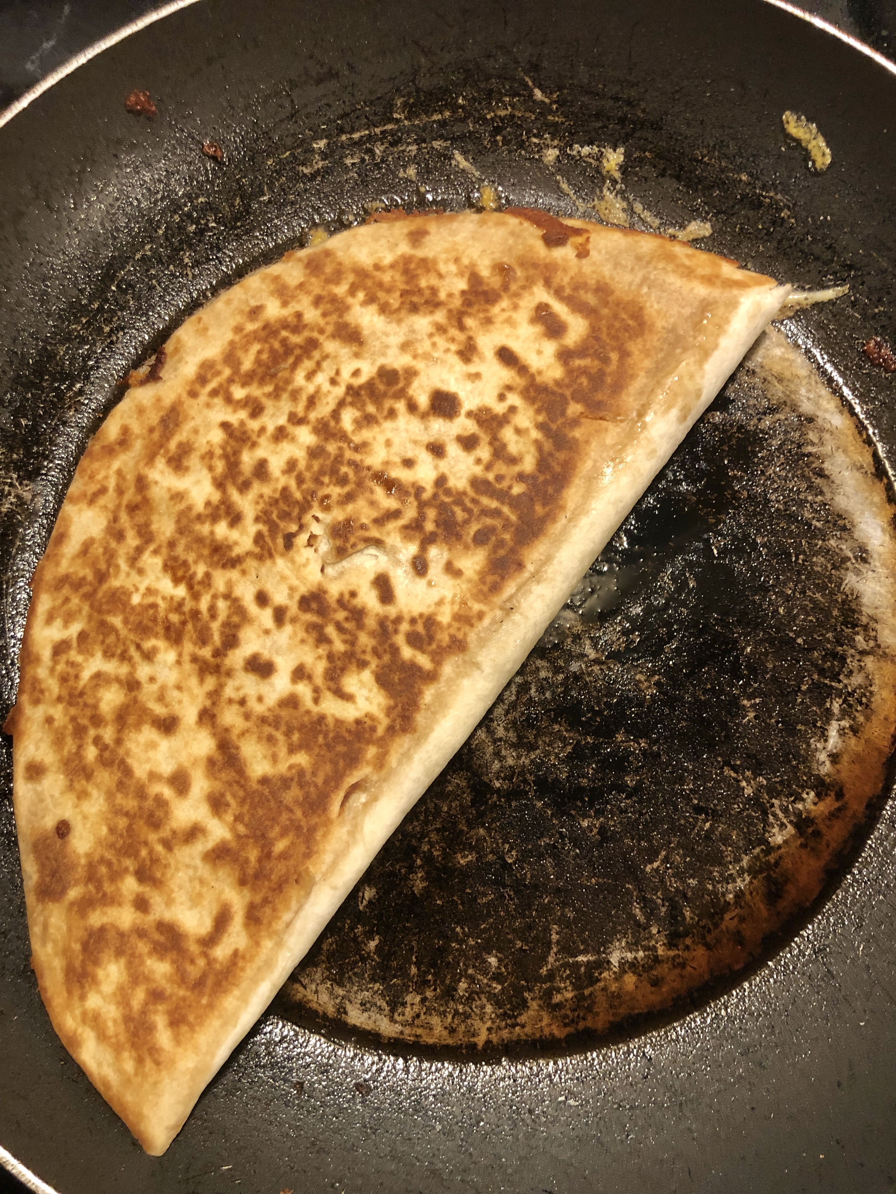 chicken quesadilla finishing cooking in pan. The quesadilla is golden brown.