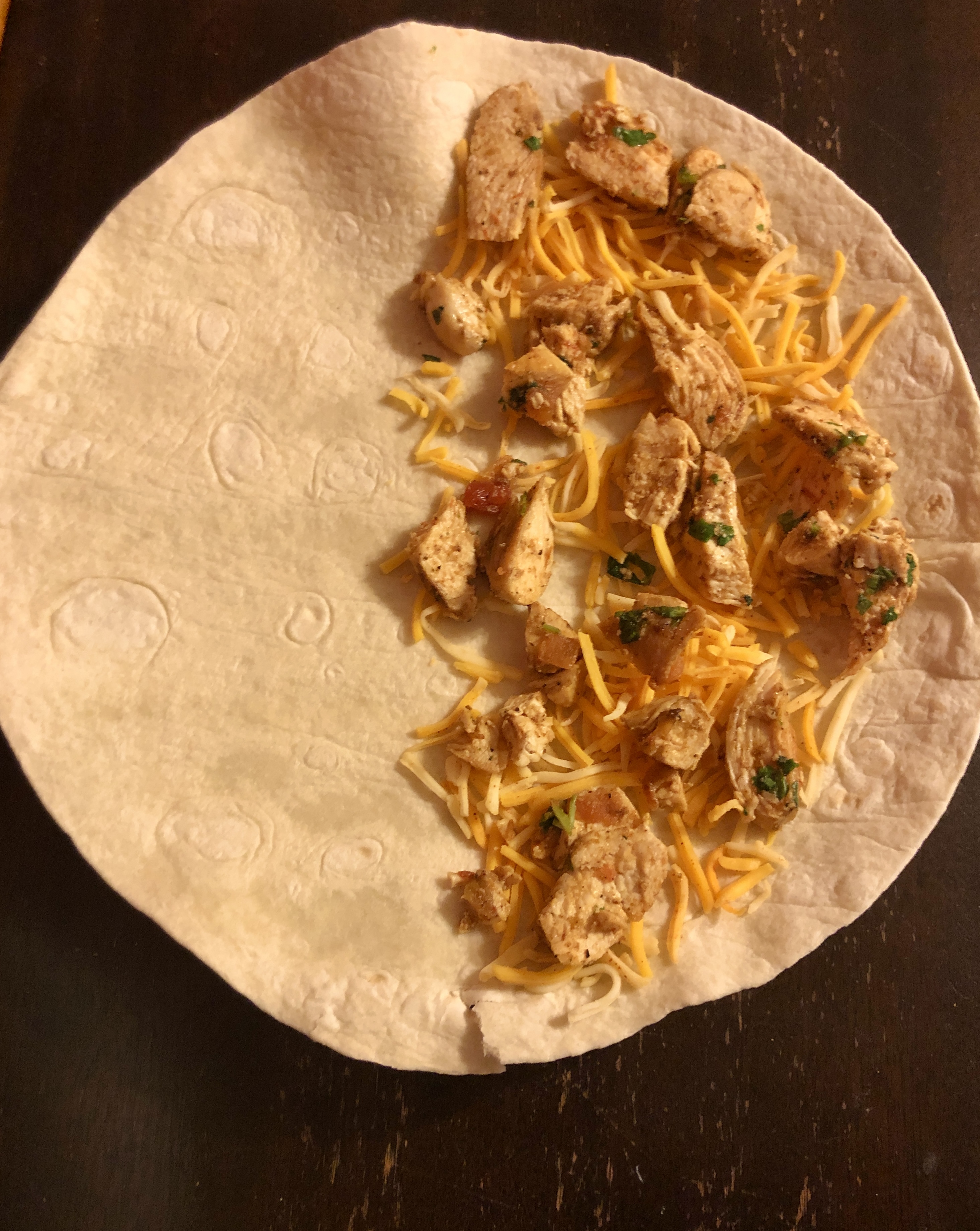 The chicken quesadilla is being assembled. Half of the flour tortilla has a layer of taco cheese topped with chicken, salsa and cilantro.