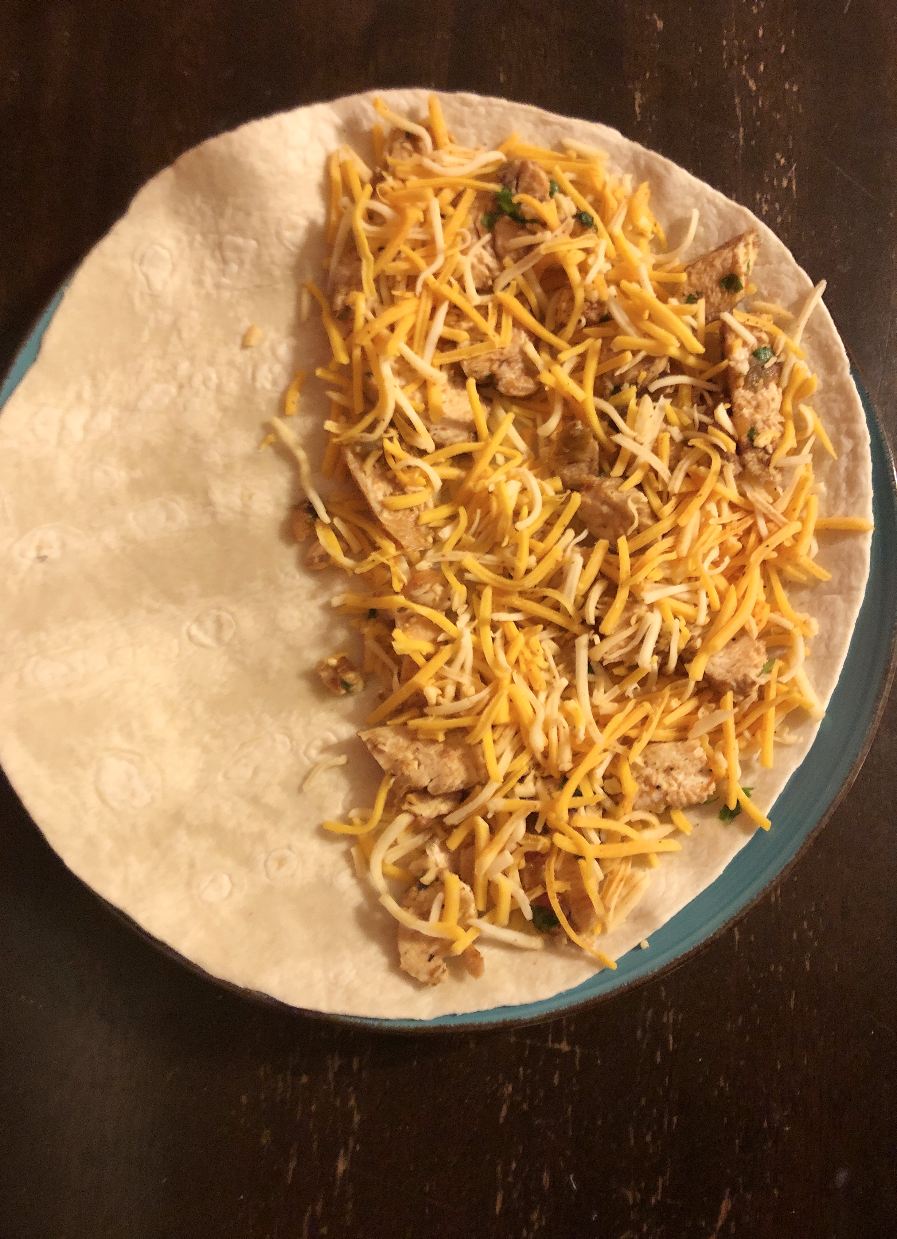 Half of a flour tortilla with taco cheese and a chicken filling is topped with additional taco cheese.