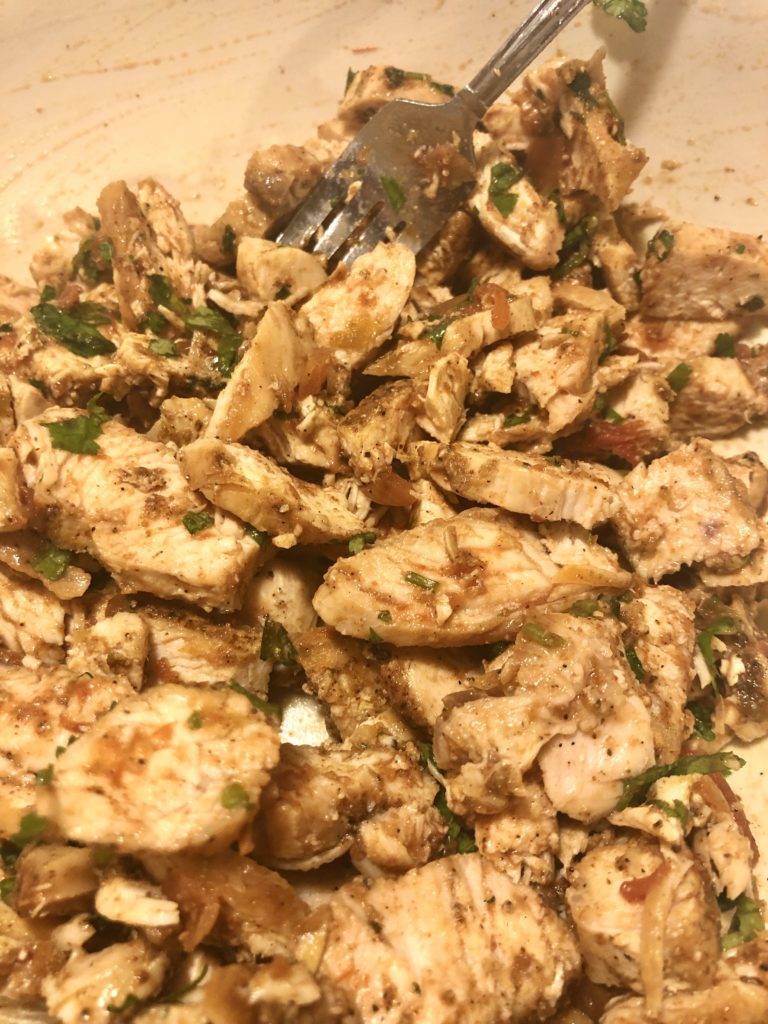 sliced cooked chicken breast mixed in bowl with salsa and cilantro