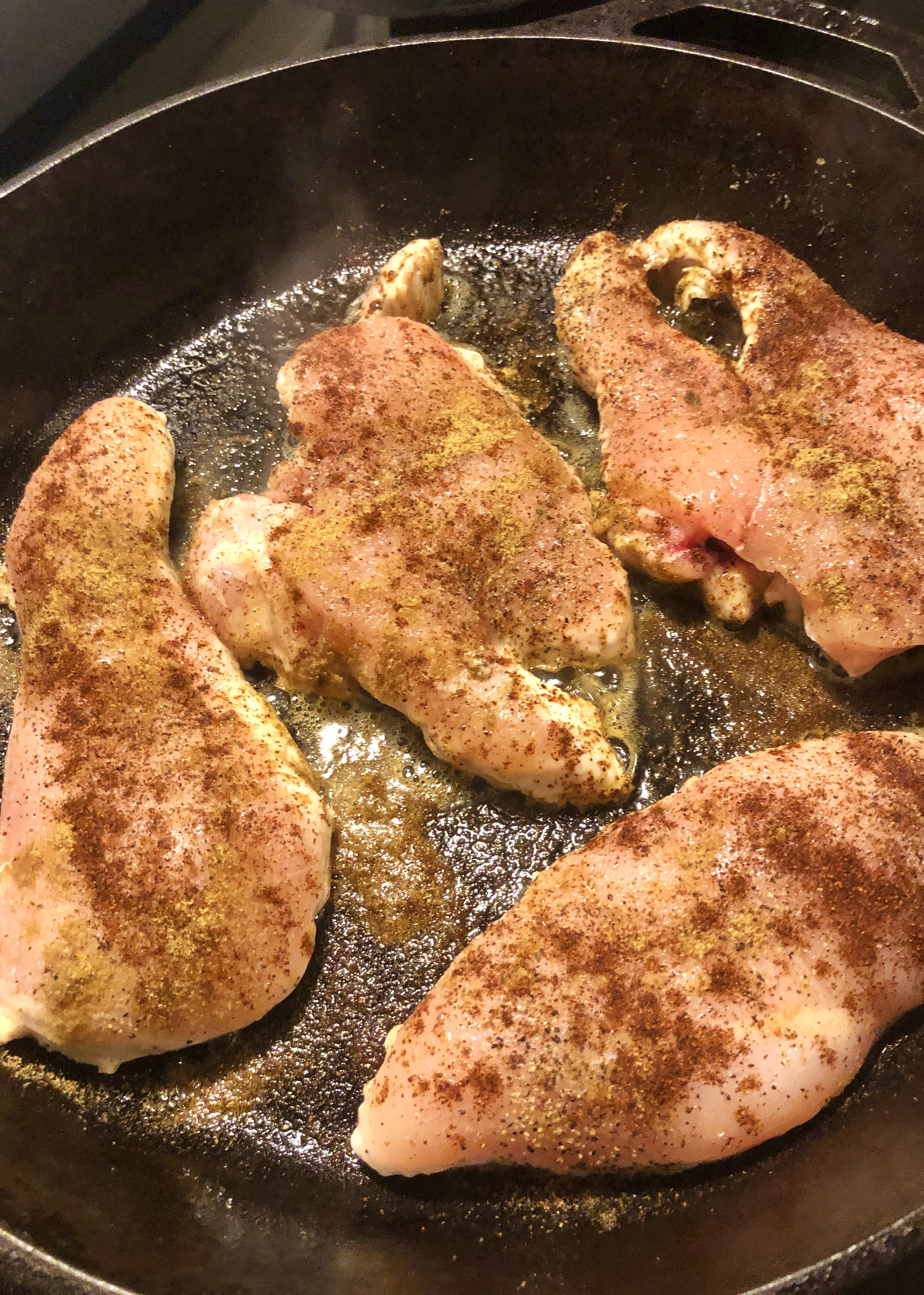 chicken breast frying in skillet with cumin and chili powder