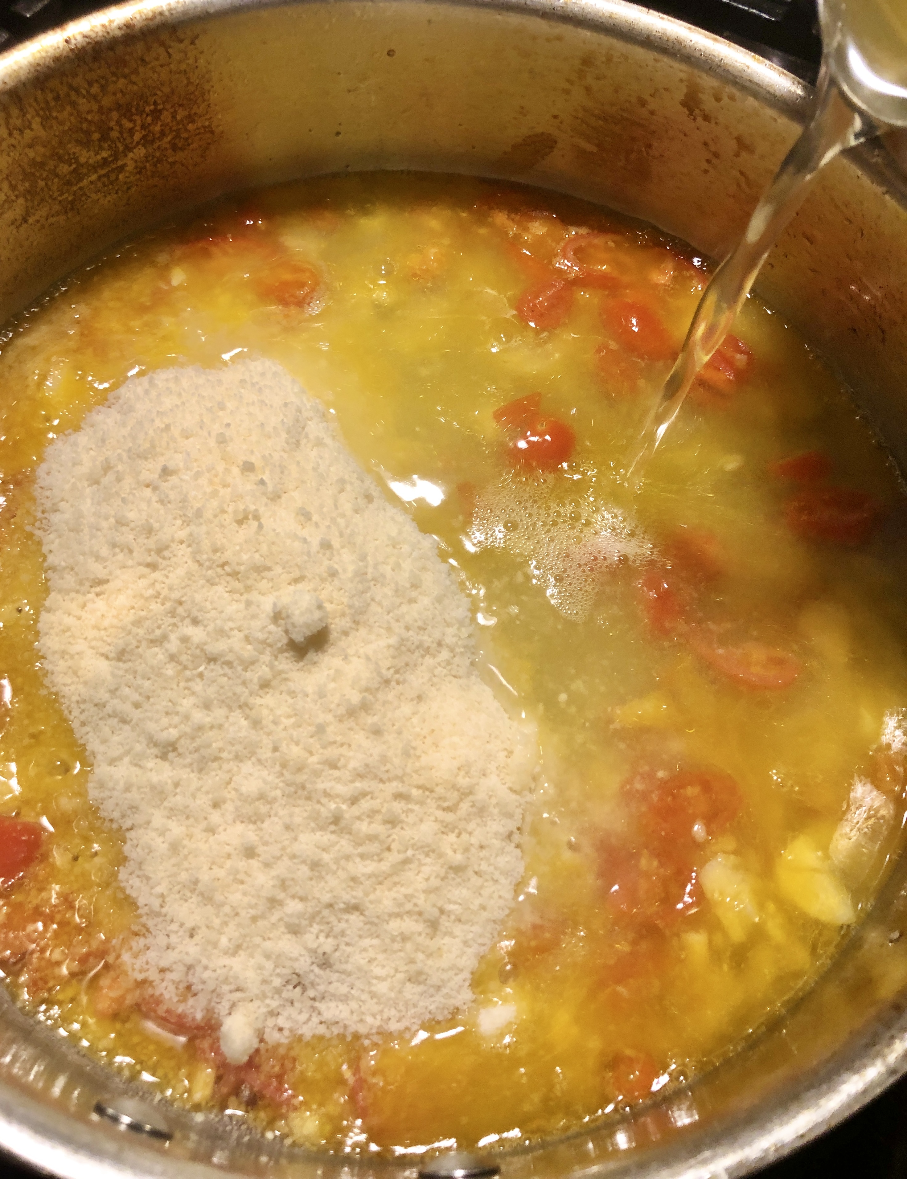 Cherry tomatoes, garlic, olive oil, butter, grated parmesan cheese in saucepan with chicken broth being poured. 