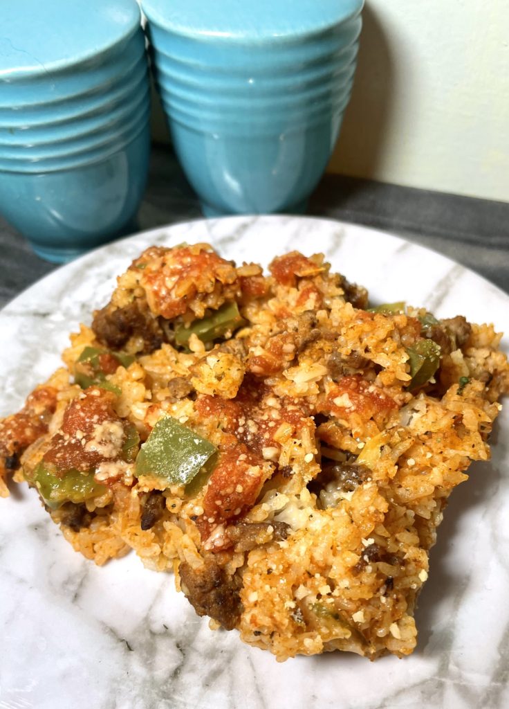 Unstuffed pepper rice casserole on a white marbled plate onto of a gray marble cutting board and pictured with large bright blue salt and pepper shakers in the background.