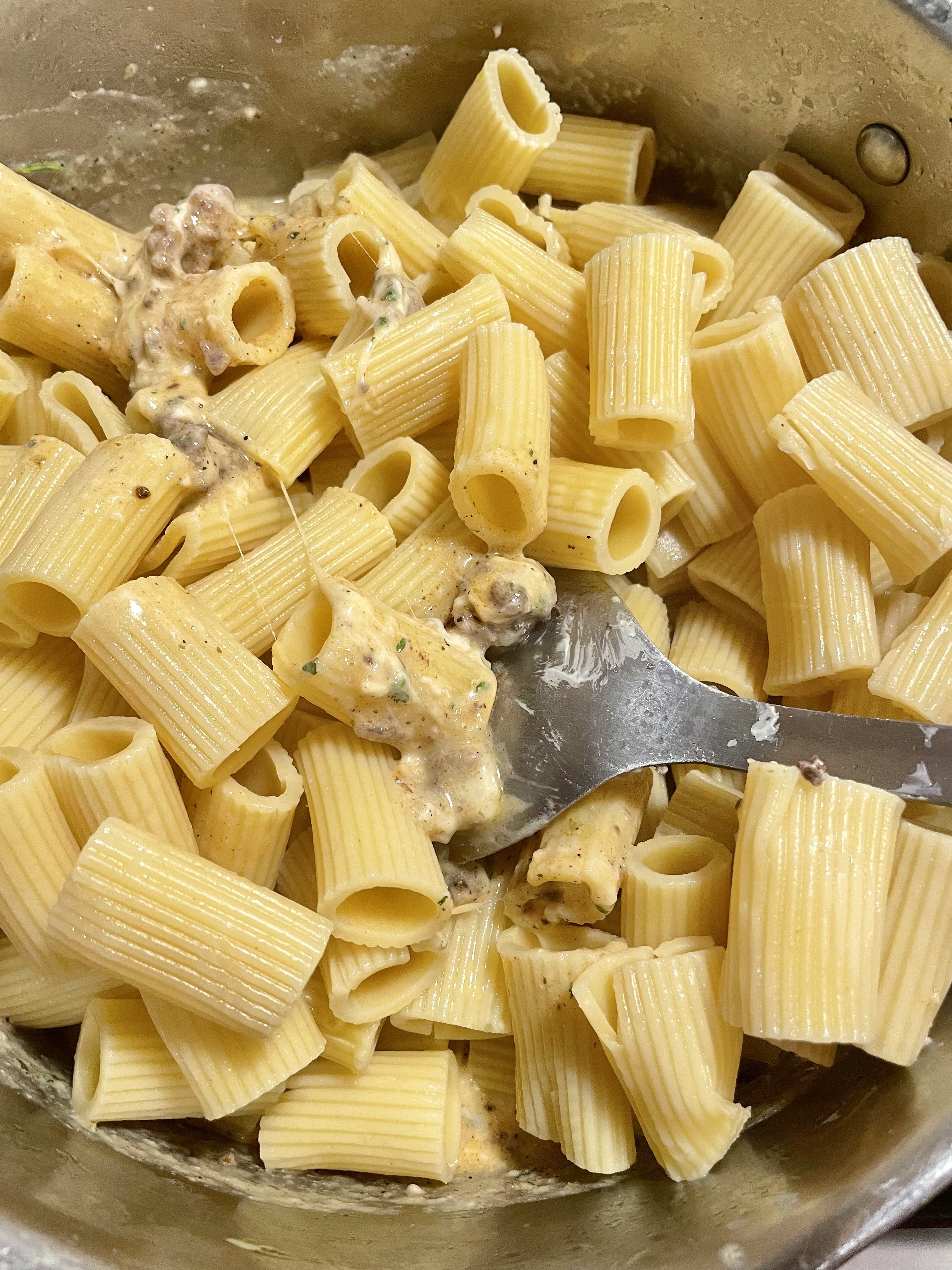Pasta in a pot with ground beef and cheese sauce beginning to be stirred to fully combine.