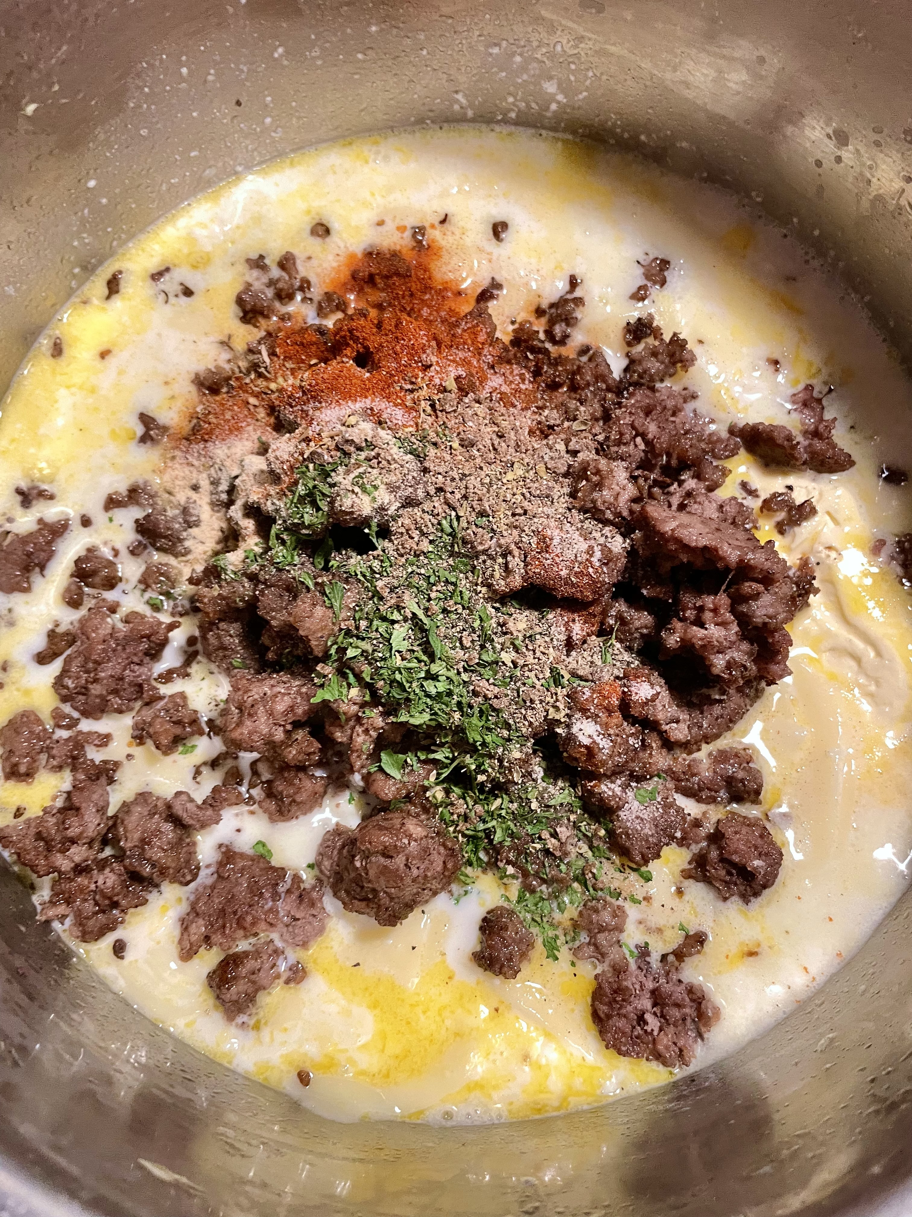 Browned ground beef and spices added to pot with cooking cheese sauce.