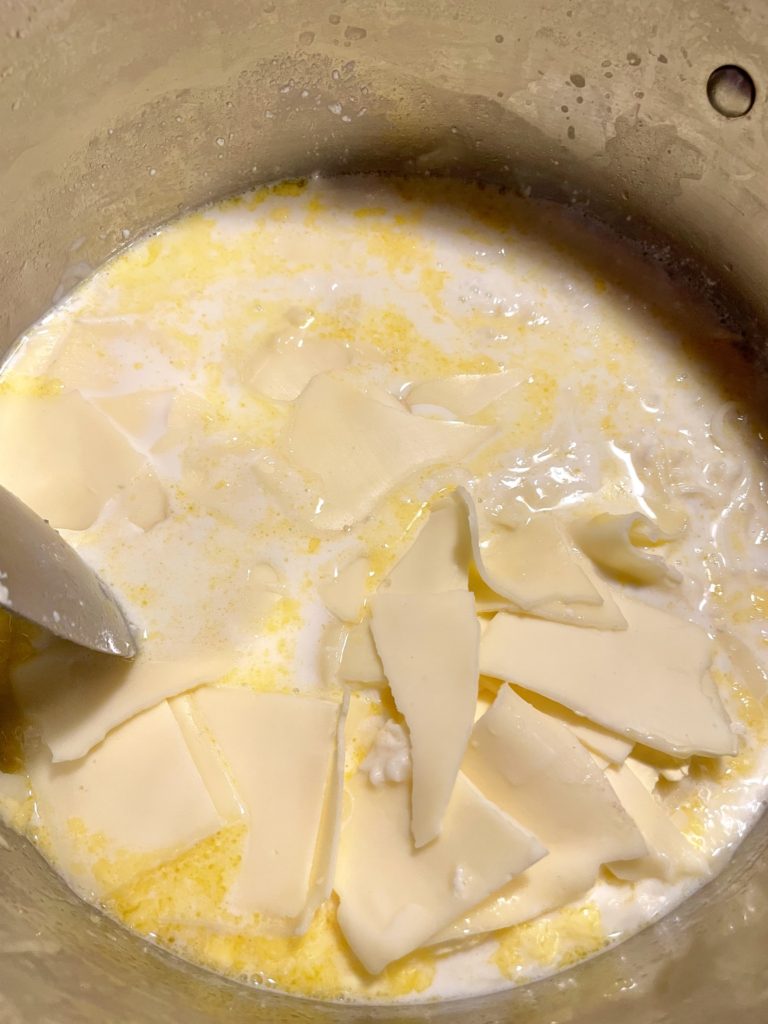 Milk, butter, mozzarella and American cheeses added to pot and being stirred to melt the cheese.