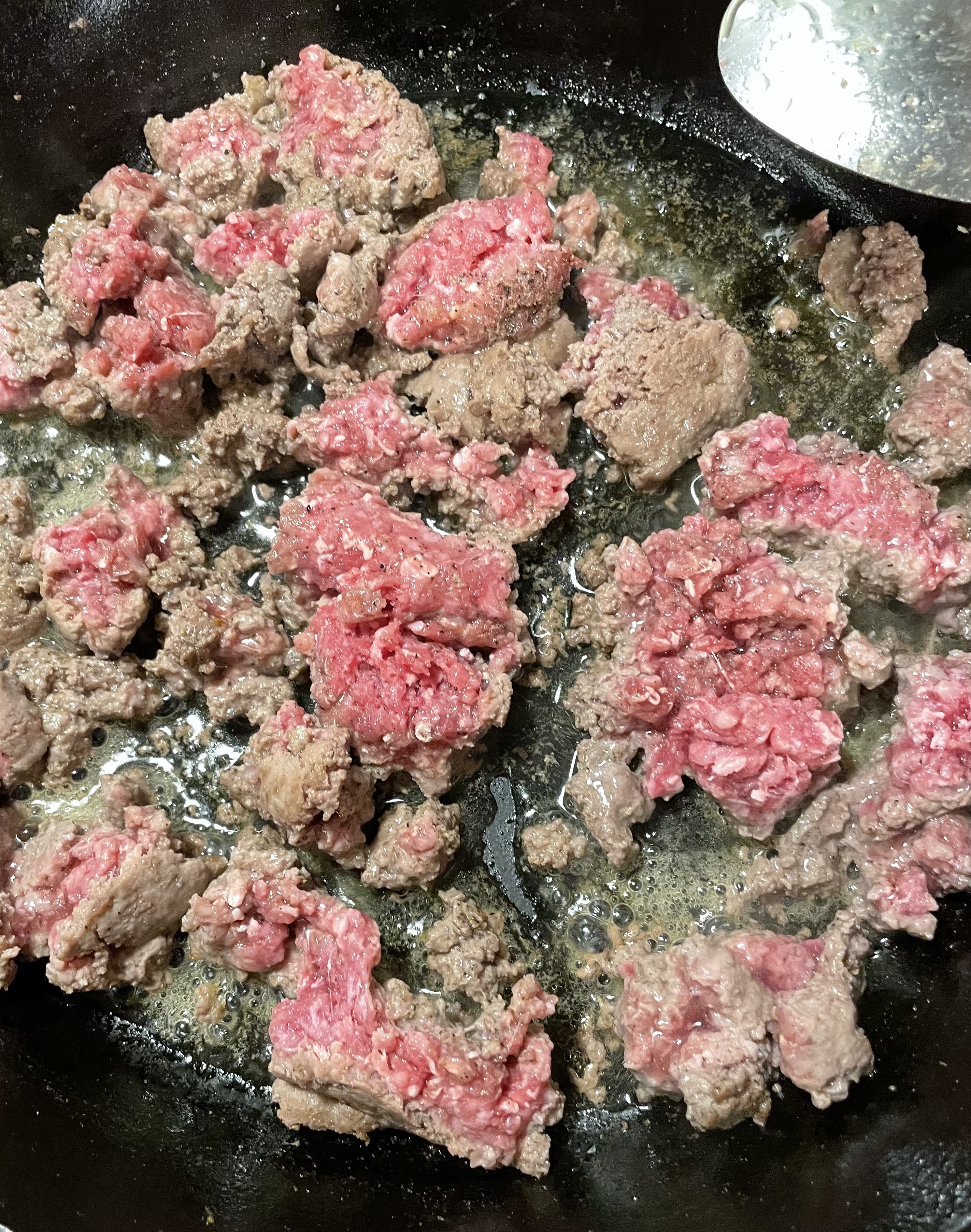 Raw ground beef being browned in a cast iron skillet.