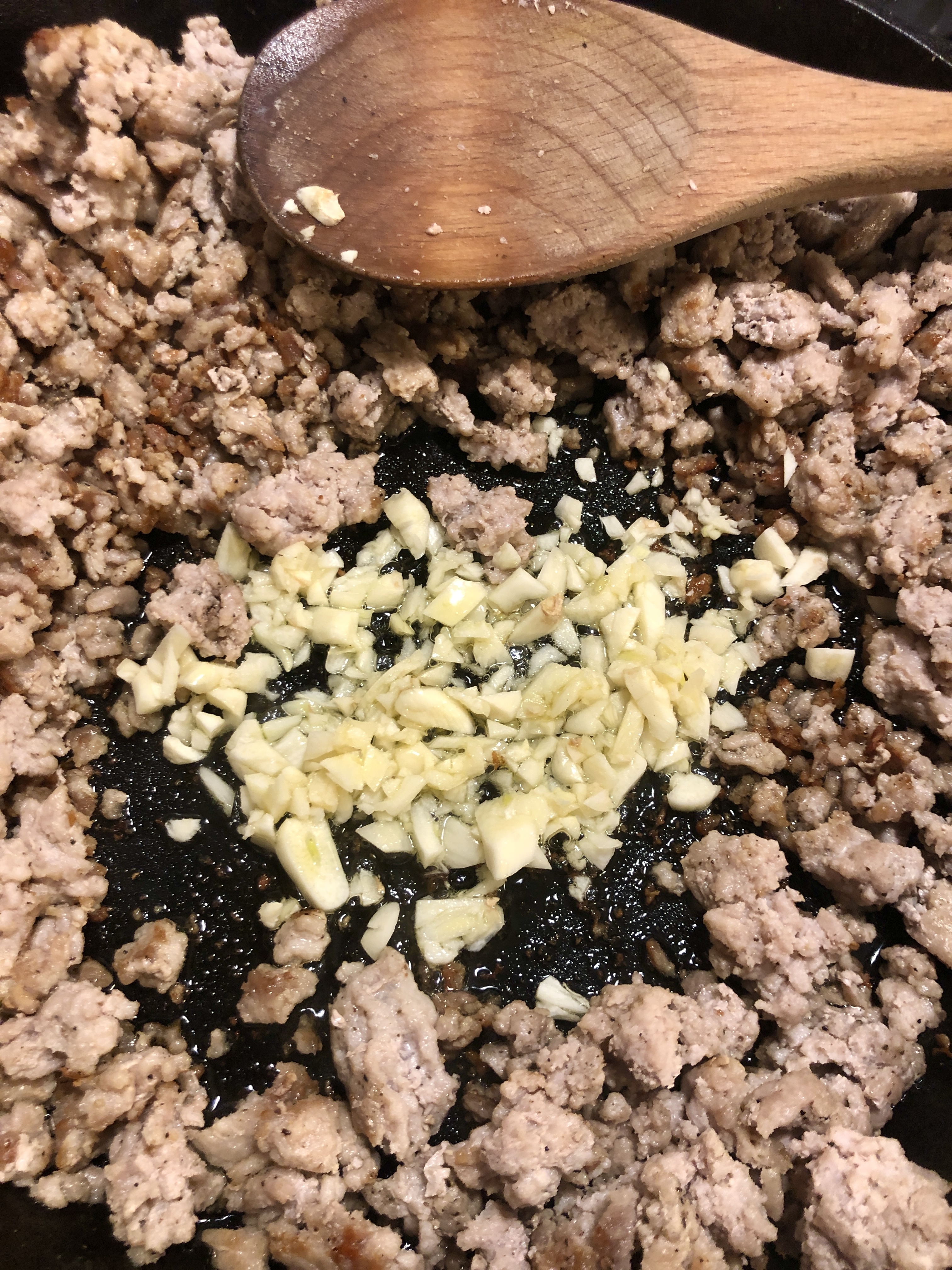 Browning ground pork in skillet and stirring with wooden spoon.