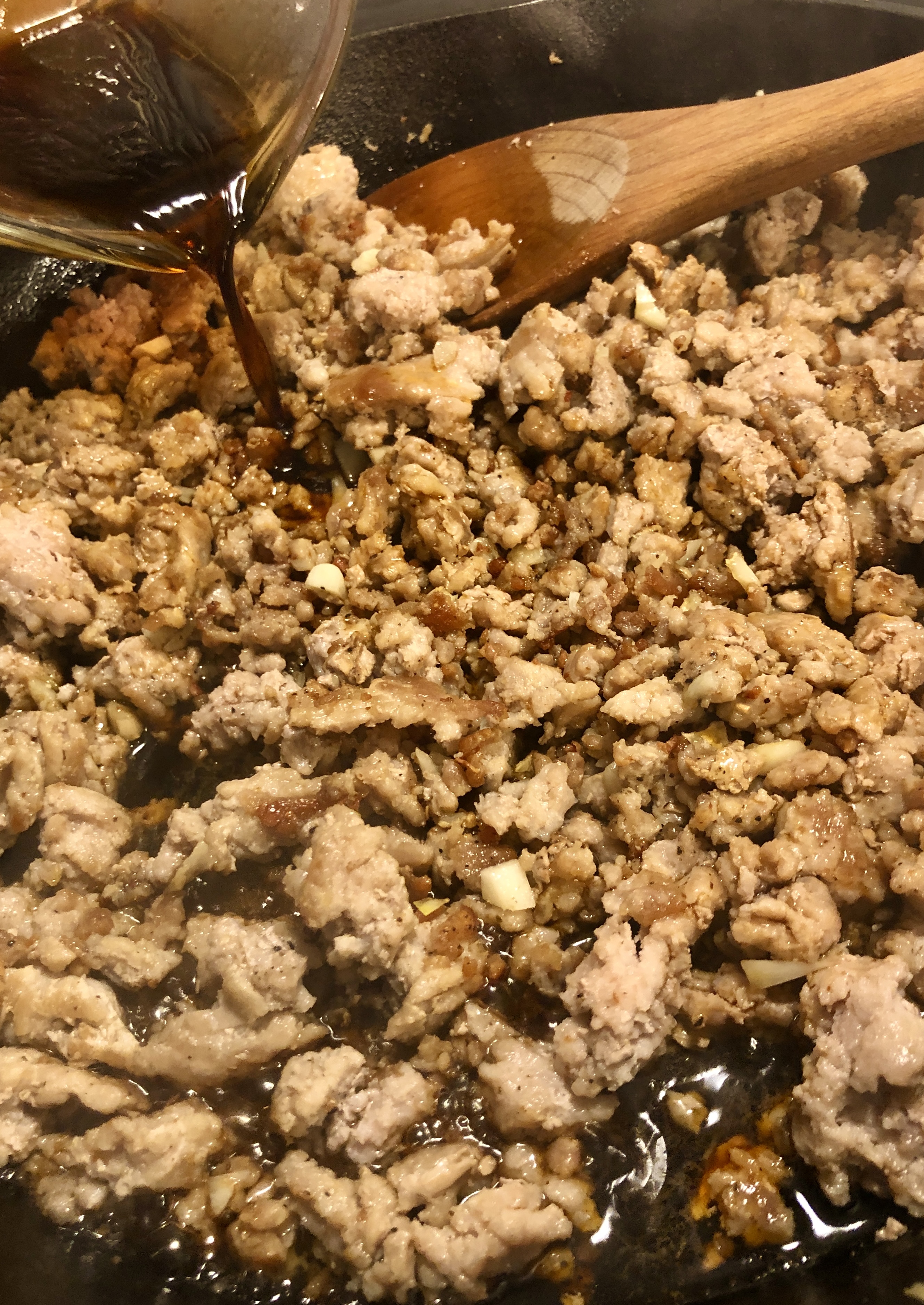 Pouring sauce into ground pork in skillet.