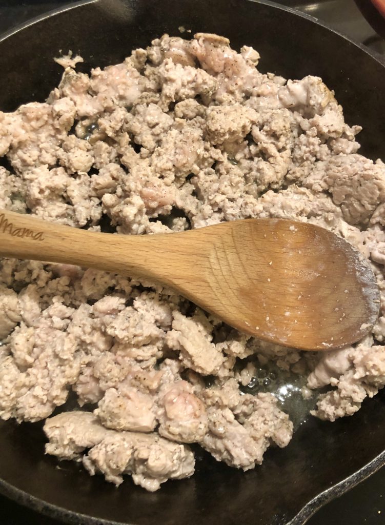 Browning ground pork in cast iron skillet and stirring with wooden spoon.