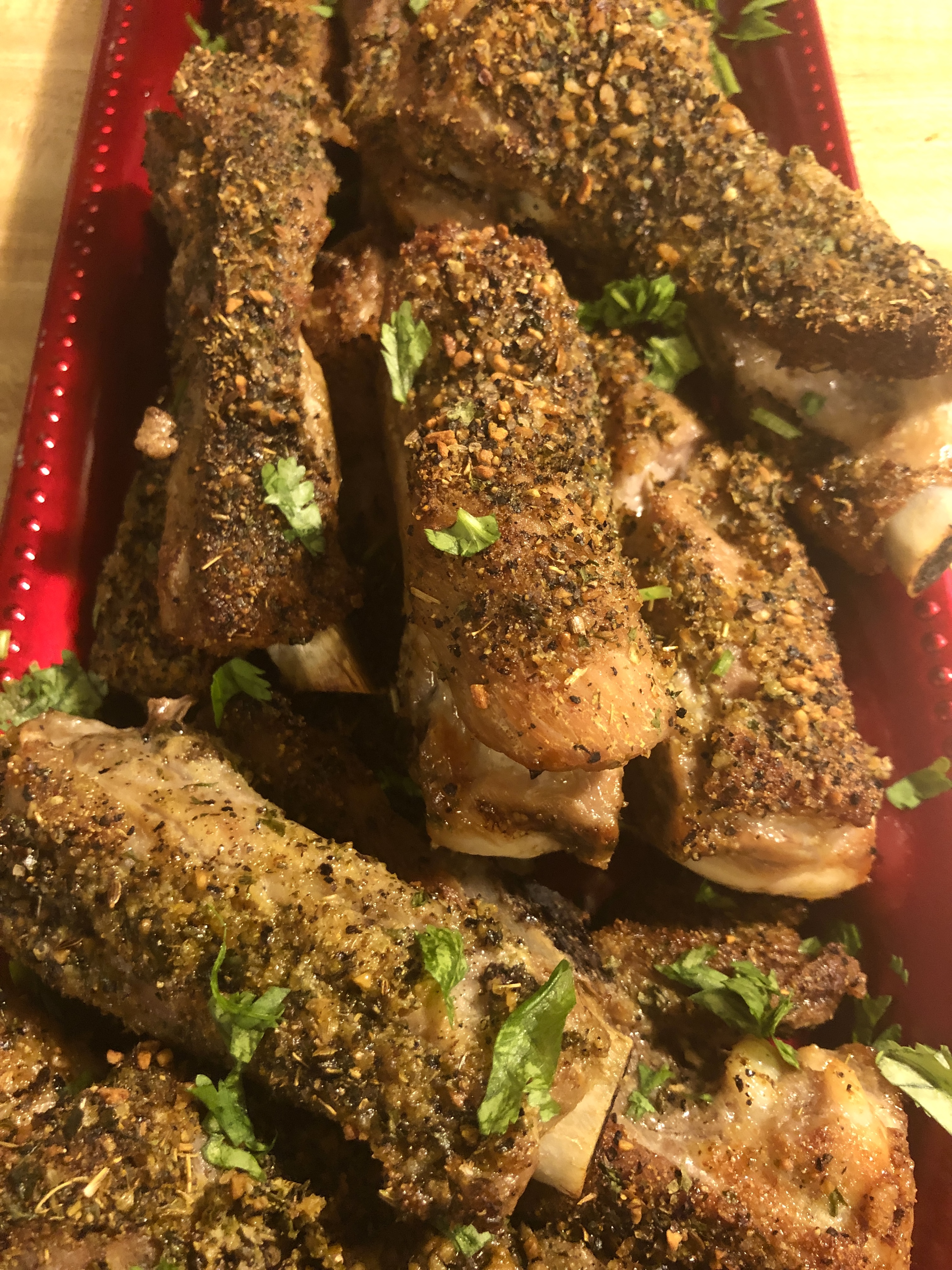 Oven baked pork ribs stacked on a red rectangle serving dish. The pork ribs are garnished with chopped cilantro.