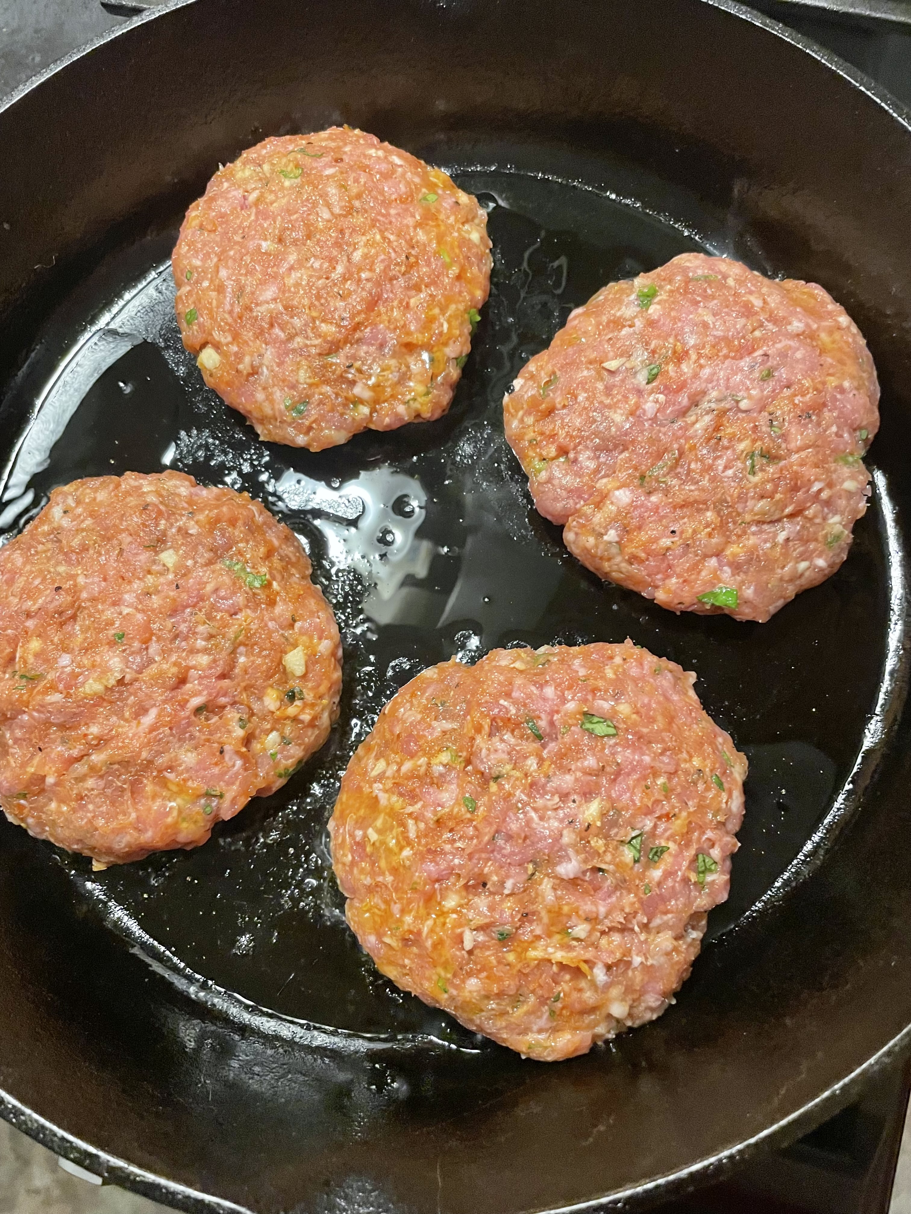 Four Thai pork burgers added to skillet on stovetop.