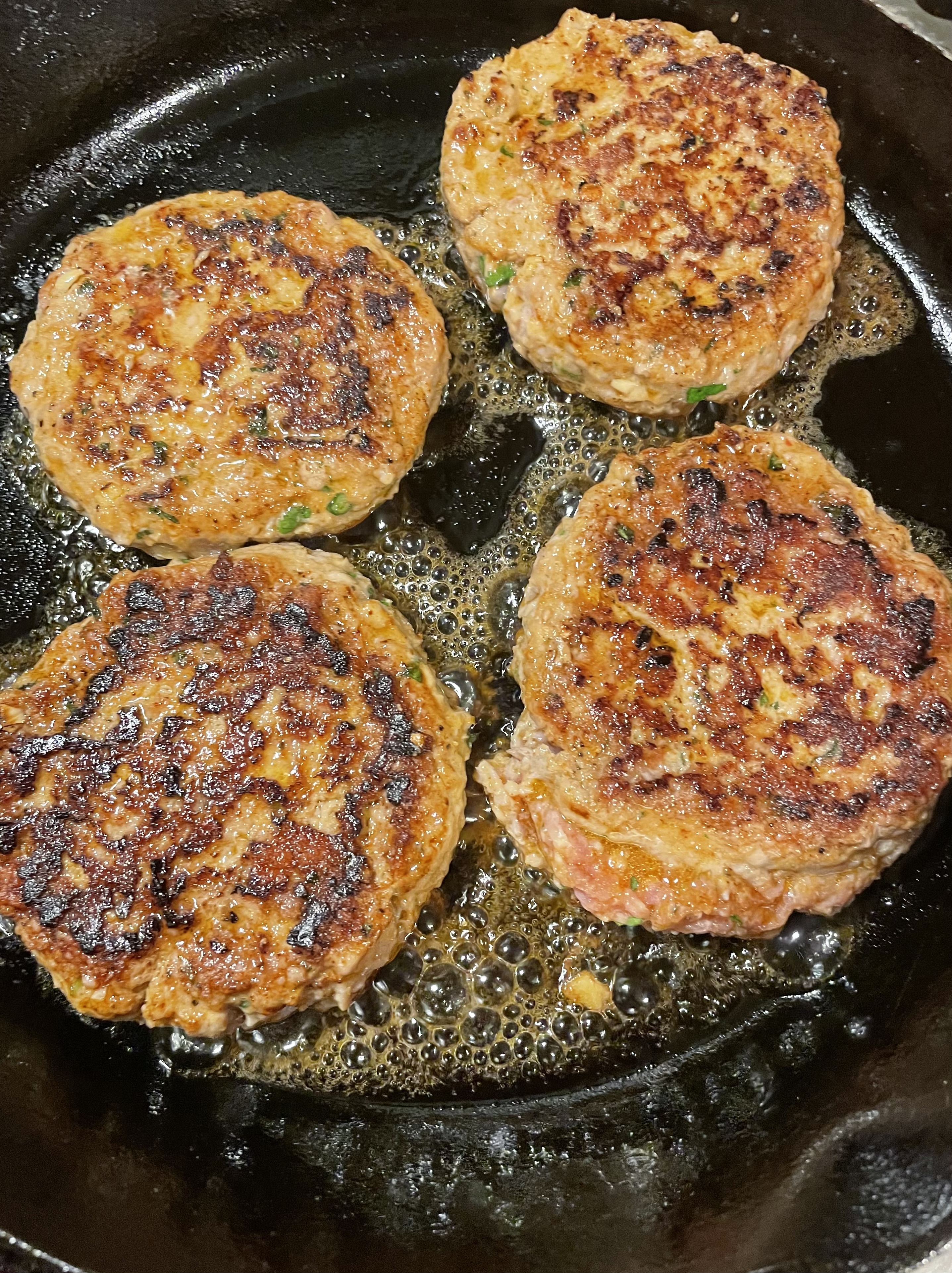 Four Thai pork burgers that have been flipped in a skillet showing that the burgers have browned.