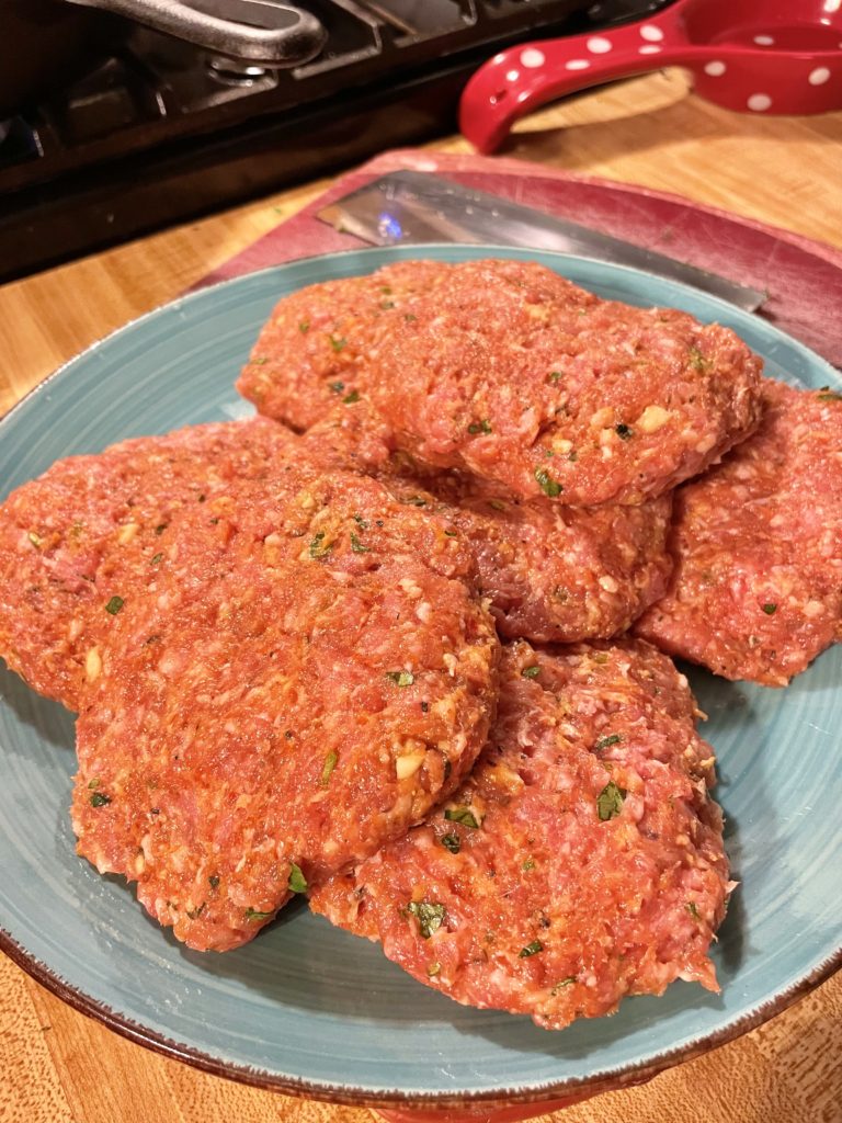 Blue plate with raw Thai pork burger patties formed.