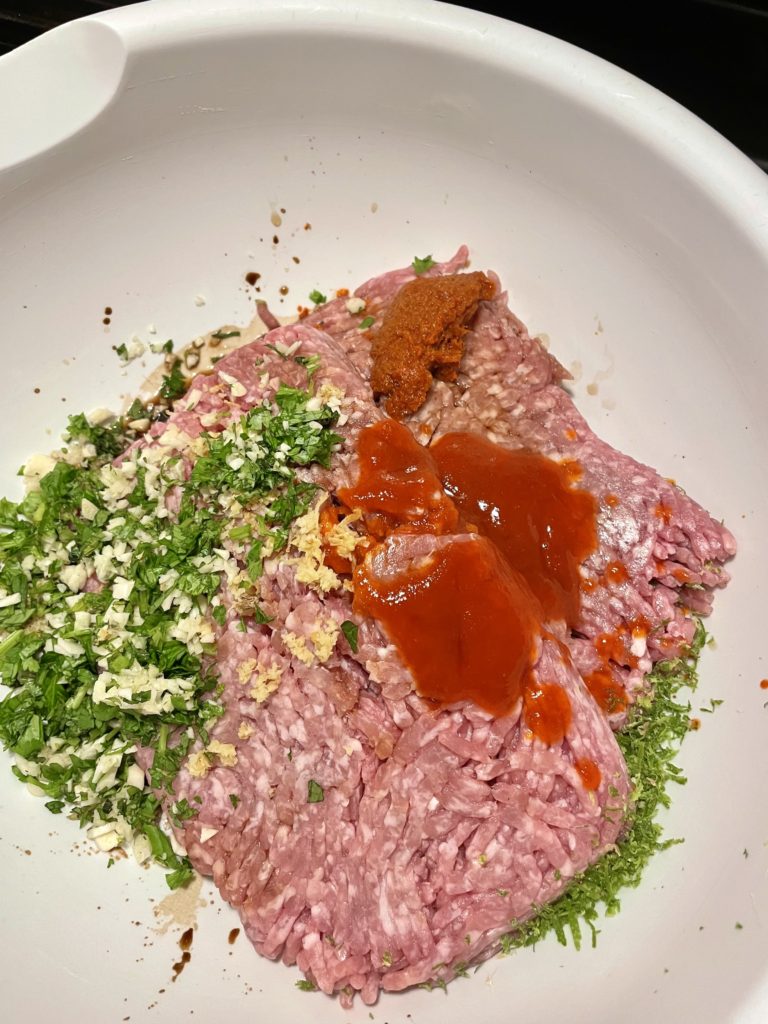 White mixing bowl with ground pork and seasonings for the best Thai pork burgers ever.