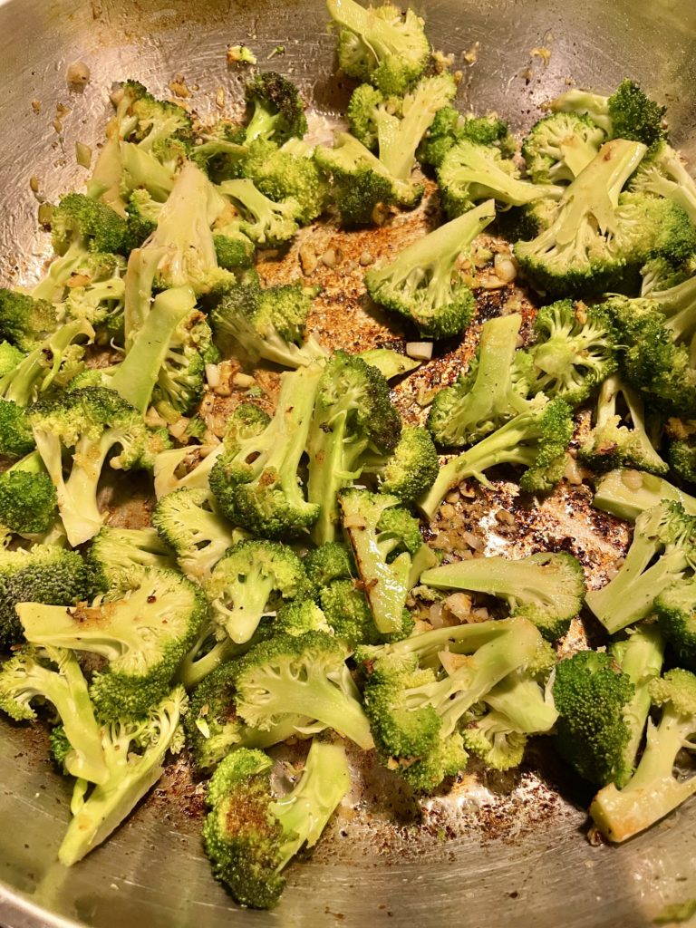 Broccoli, ginger, green onion and garlic frying with vegetable oil in a large skillet.