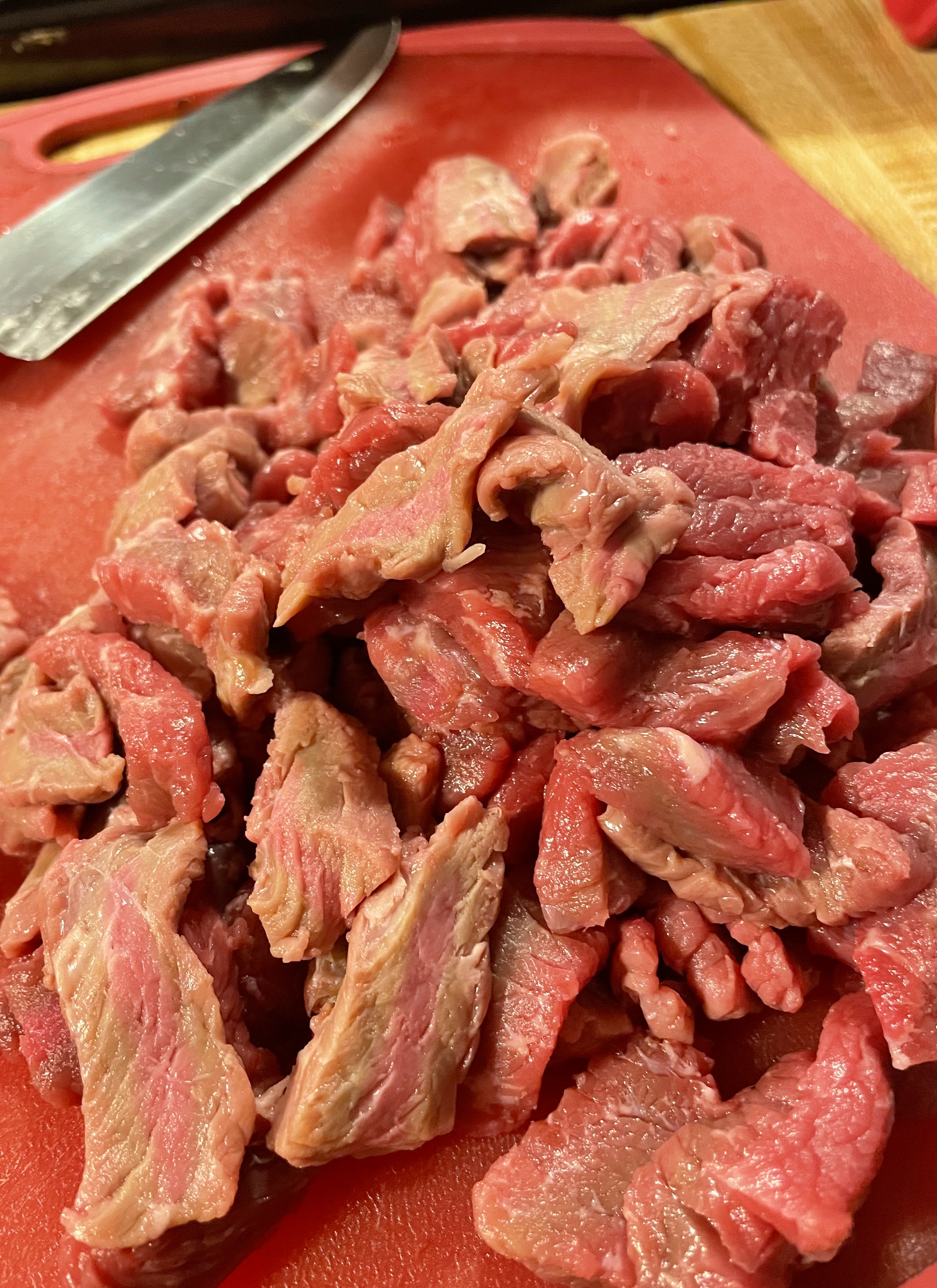 Thinly sliced beef of red cutting board with a knife beside it.