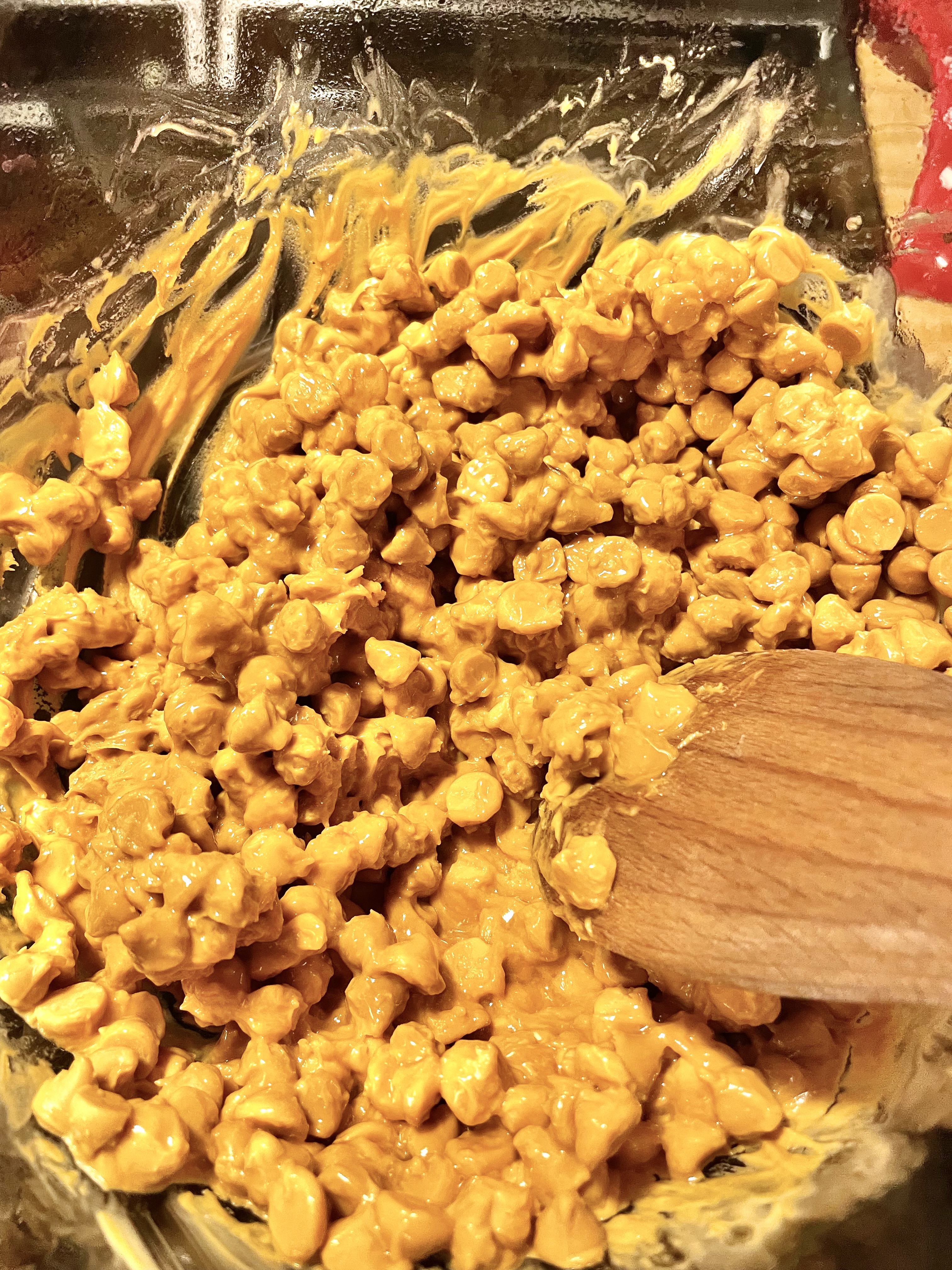 Butterscotch chips added to double boiler and being stirred with a wooden spoon.
