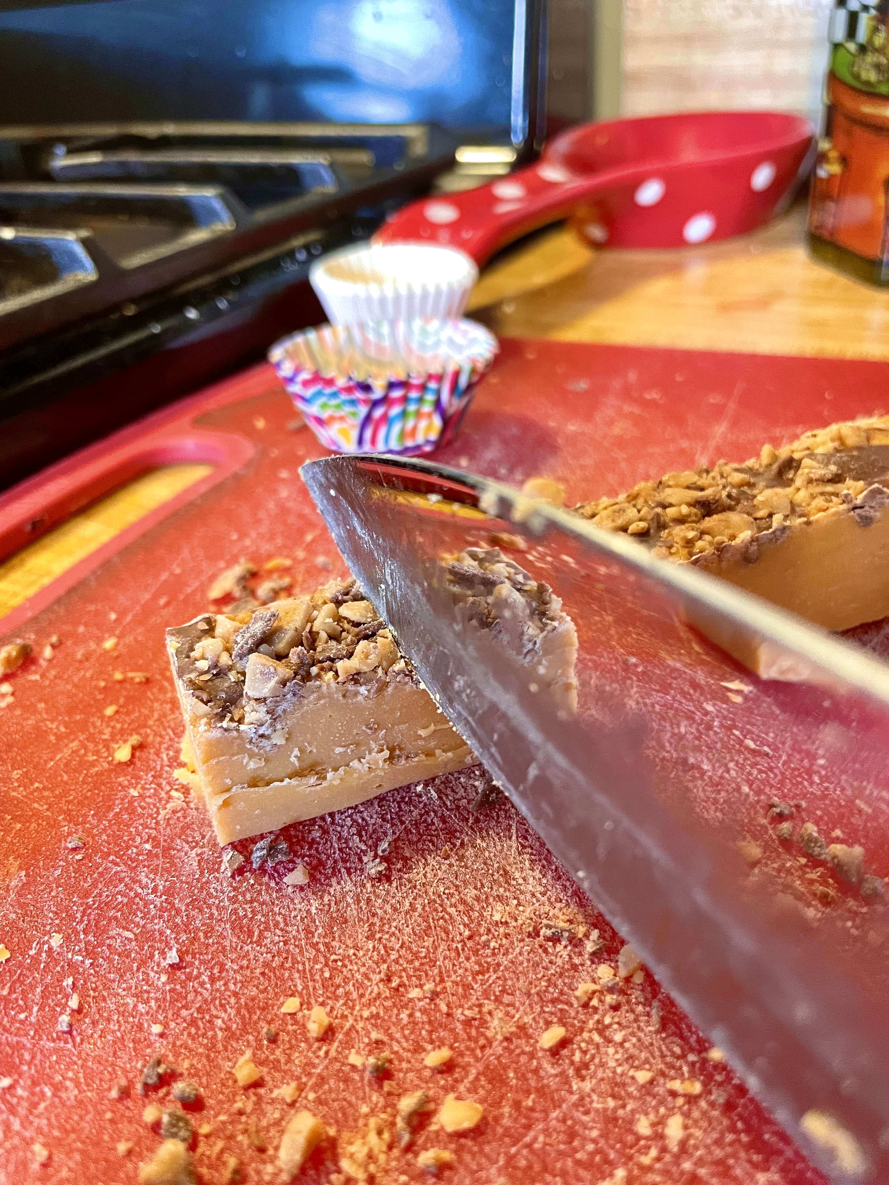 Butterscotch Toffee Heath Fudge being sliced into squares on a red cutting board.
