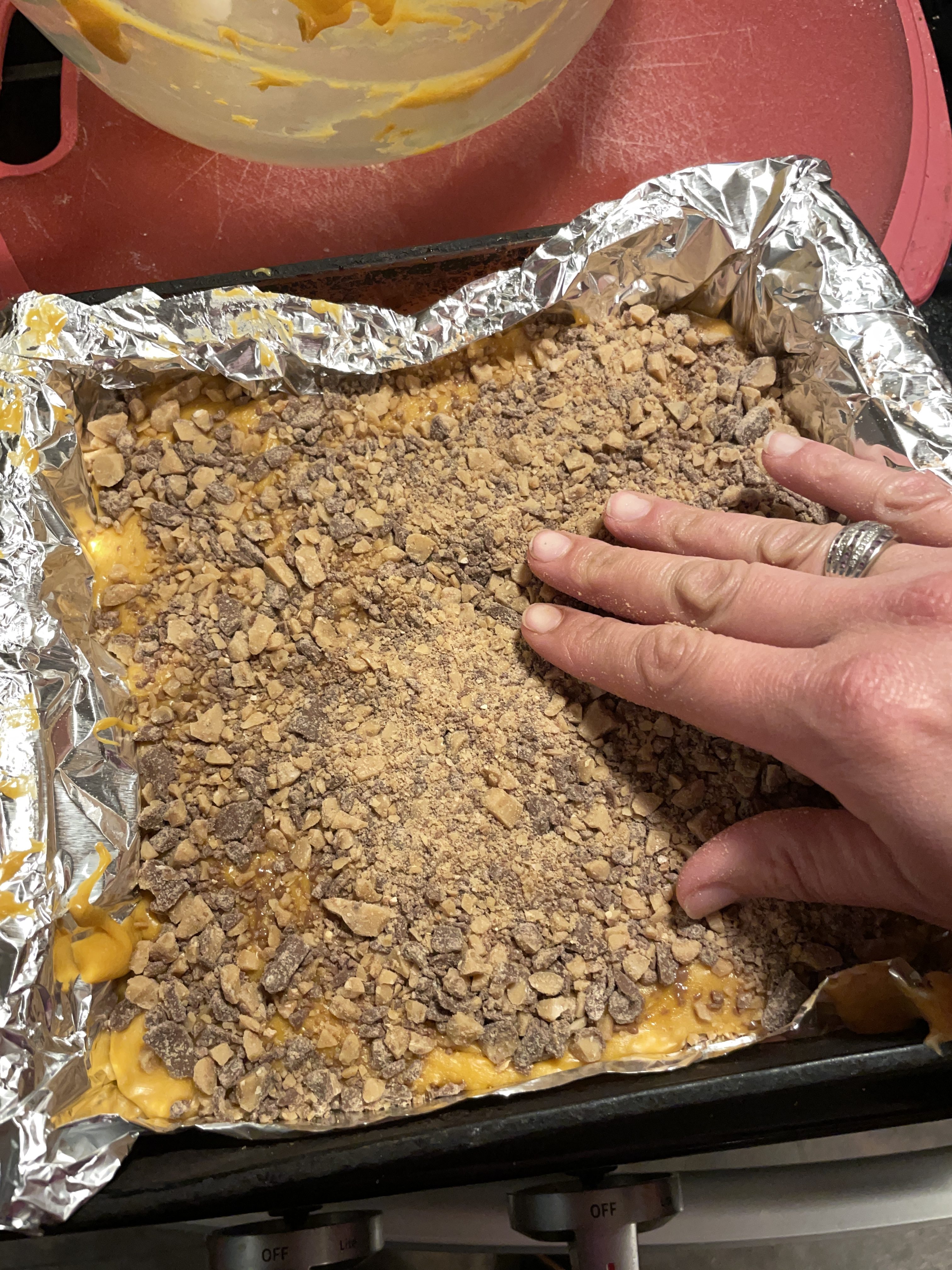 Butterscotch fudge in baking dish with Heath English Toffee bits being gently pressed into the top.