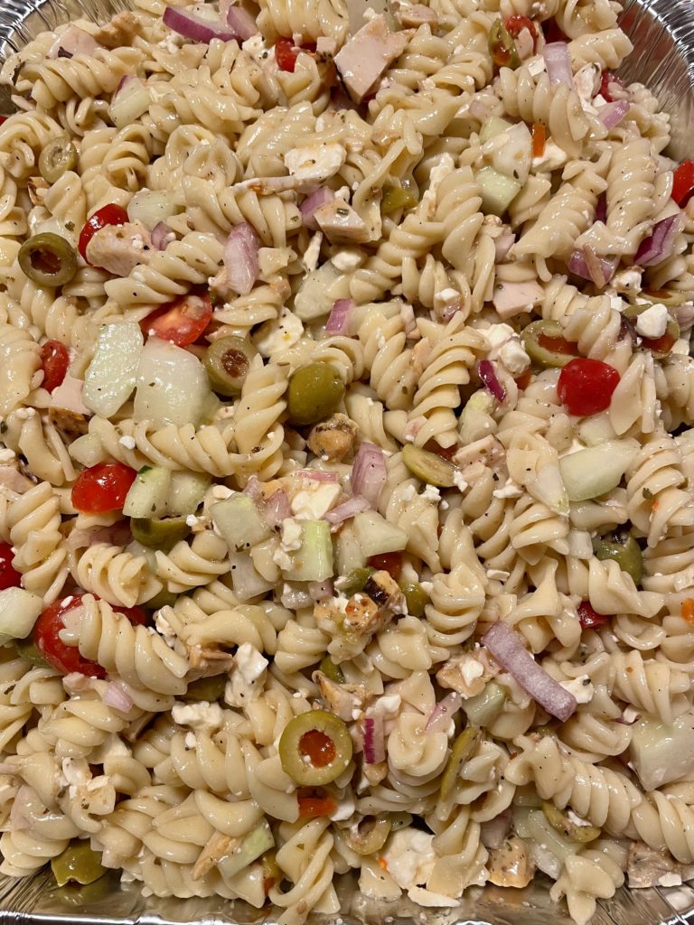 Greek pasta salad with grilled chicken pictured overhead in a foil tray.